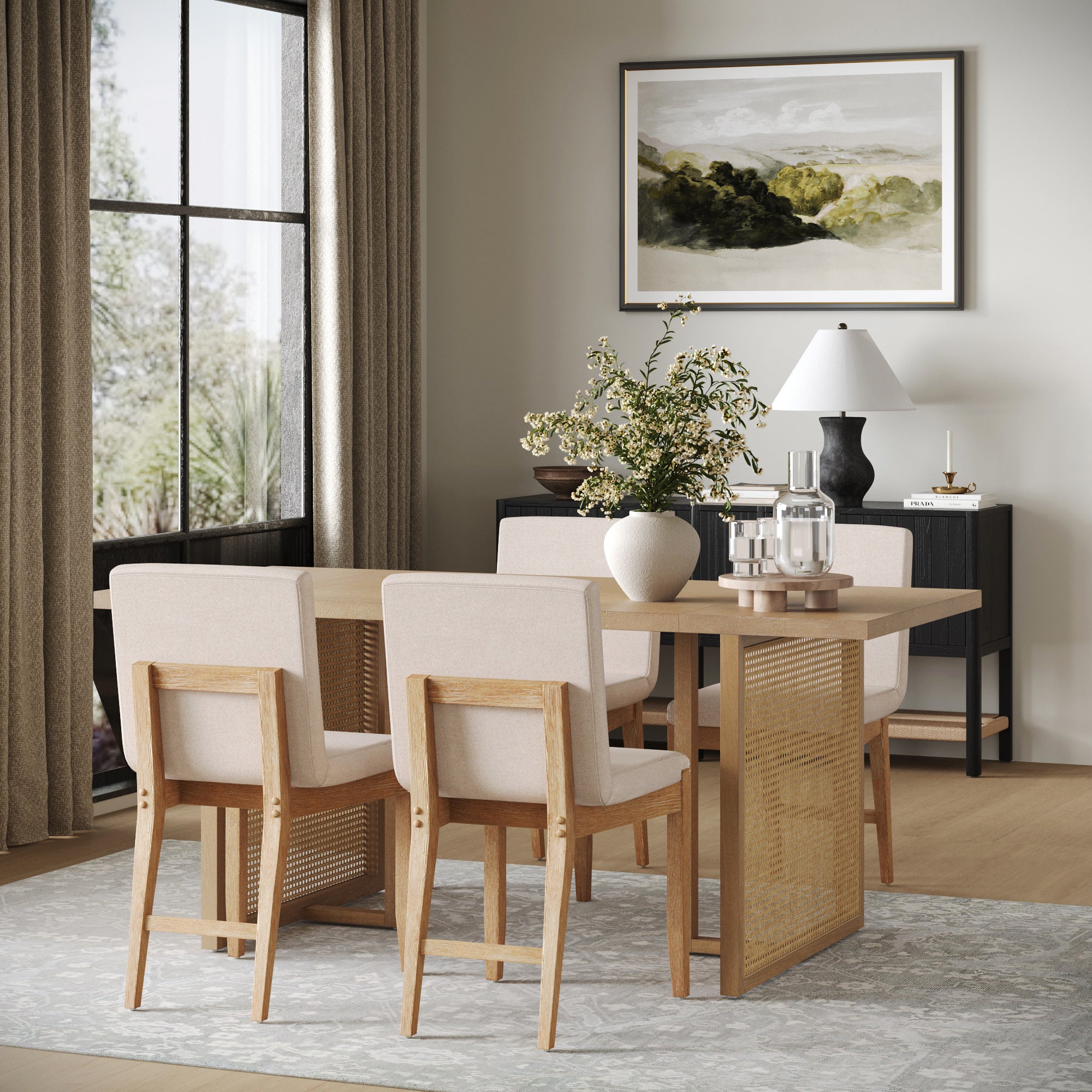Modern dining room featuring the Nathan James Rattan Boho Dining Set with 4 upholstered chairs, a vase with greenery, table lamp, and wall art. Large window with sheer curtains adds natural light to the minimalist, neutral-toned decor.