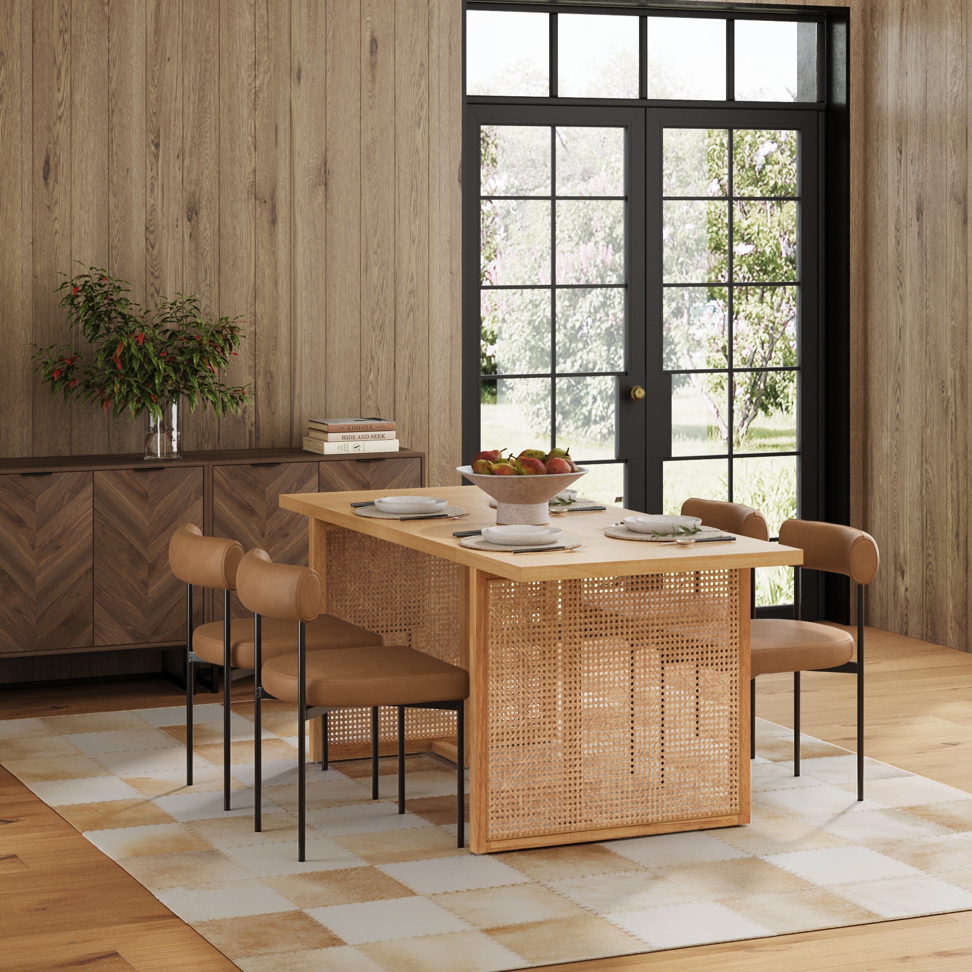 A modern dining room features the Nathan James Mid-Century Faux Leather Dining Set with four chairs, a fruit bowl and plates on the table, a sideboard with a vase of greenery, and large windows bathing the space in natural light.