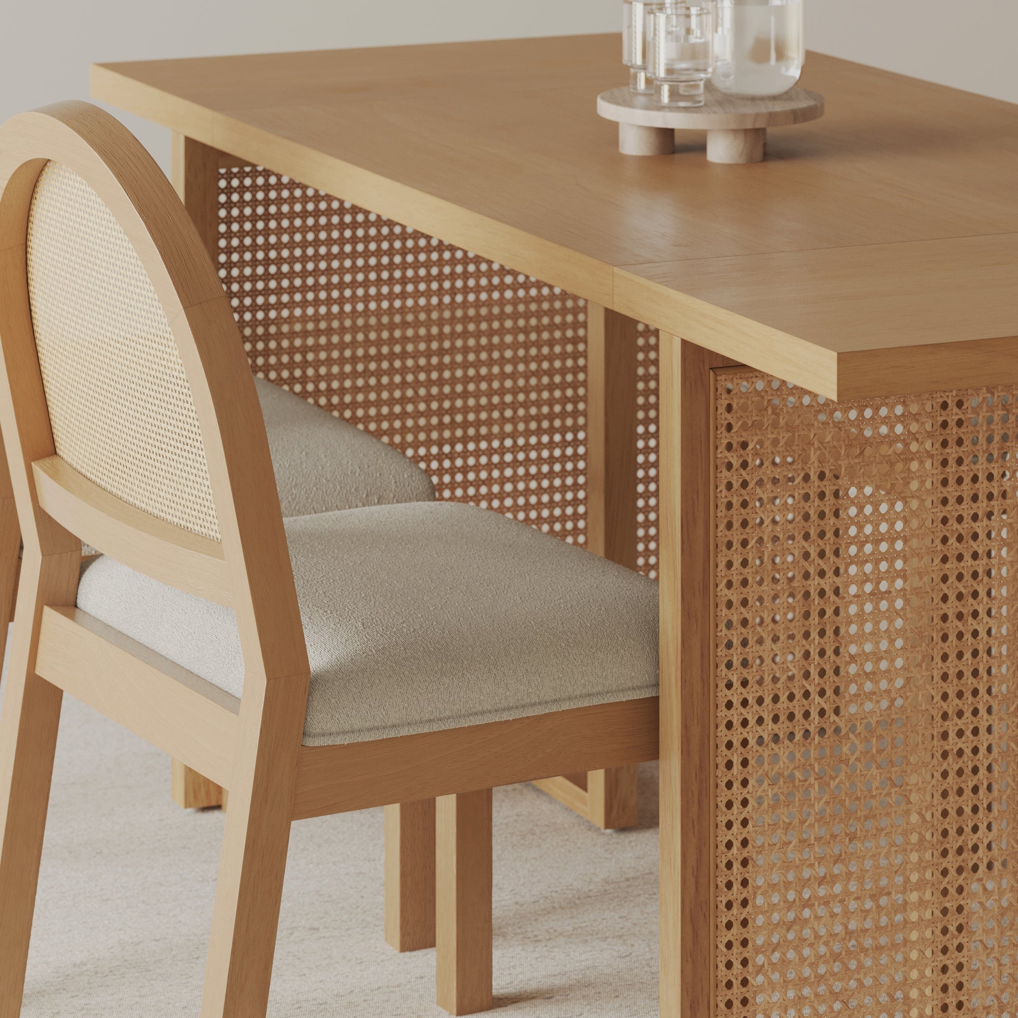 A wooden desk with woven cane panels is paired with a matching chair that has a rounded back and light fabric seat. Two glasses of water sit on a round wooden coaster on the desk.
