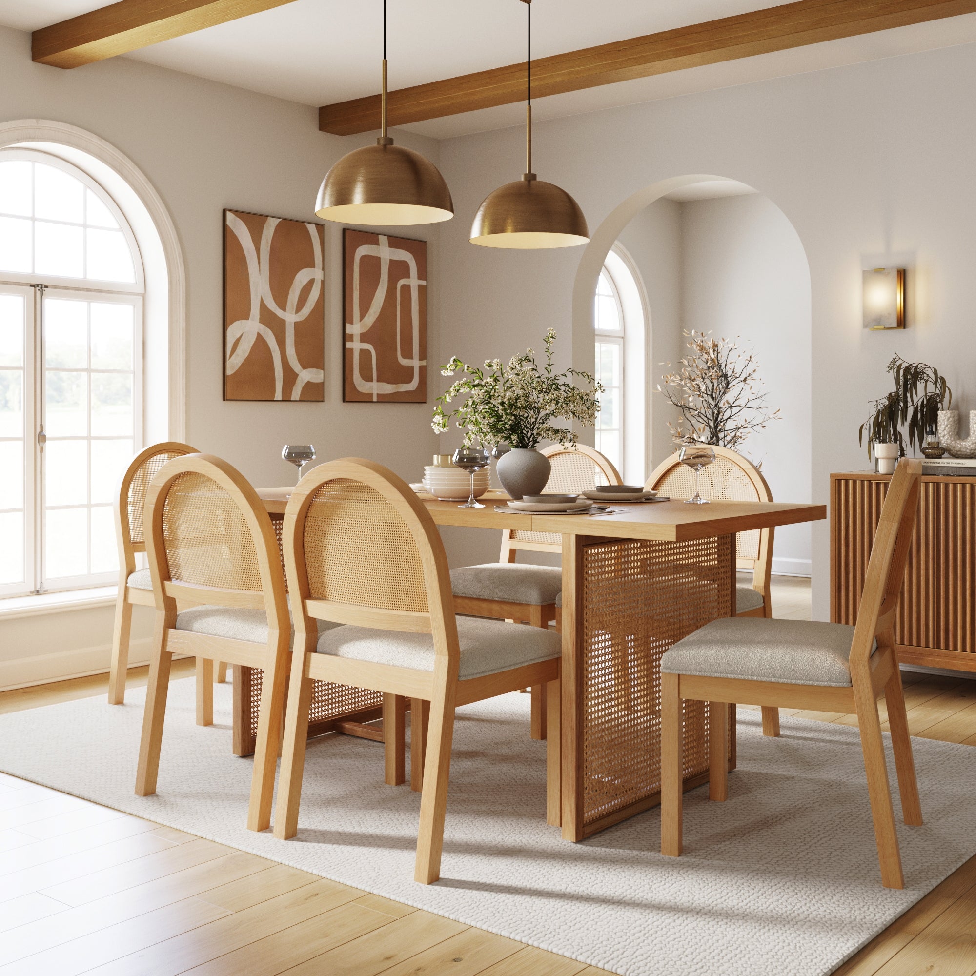 A bright, modern dining room features the Nathan James Bohemian Rattan & Boucle Dining Set with six chairs, a solid wood table, pendant lighting, abstract wall art, arched windows, plants, and neutral tones enhanced by natural light.