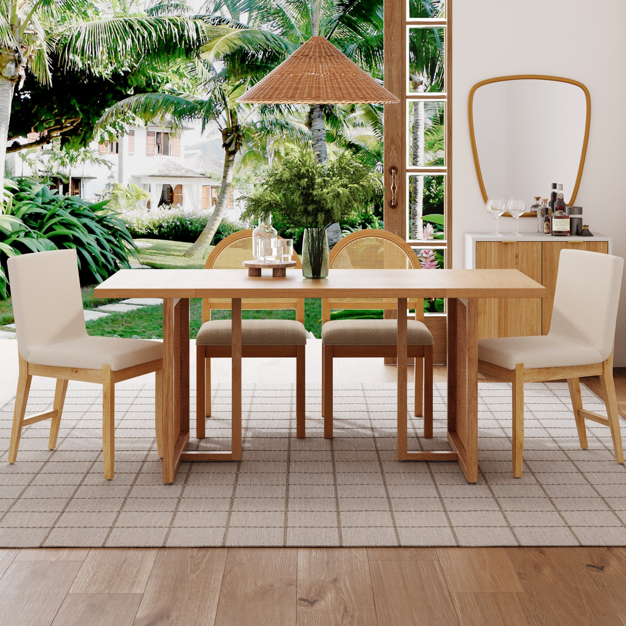 A modern dining room with a wooden table, four cream-colored chairs, a vase of greenery, and large windows showing a lush tropical garden outside. A bar cart and mirror are against the wall, and a woven pendant light hangs above.