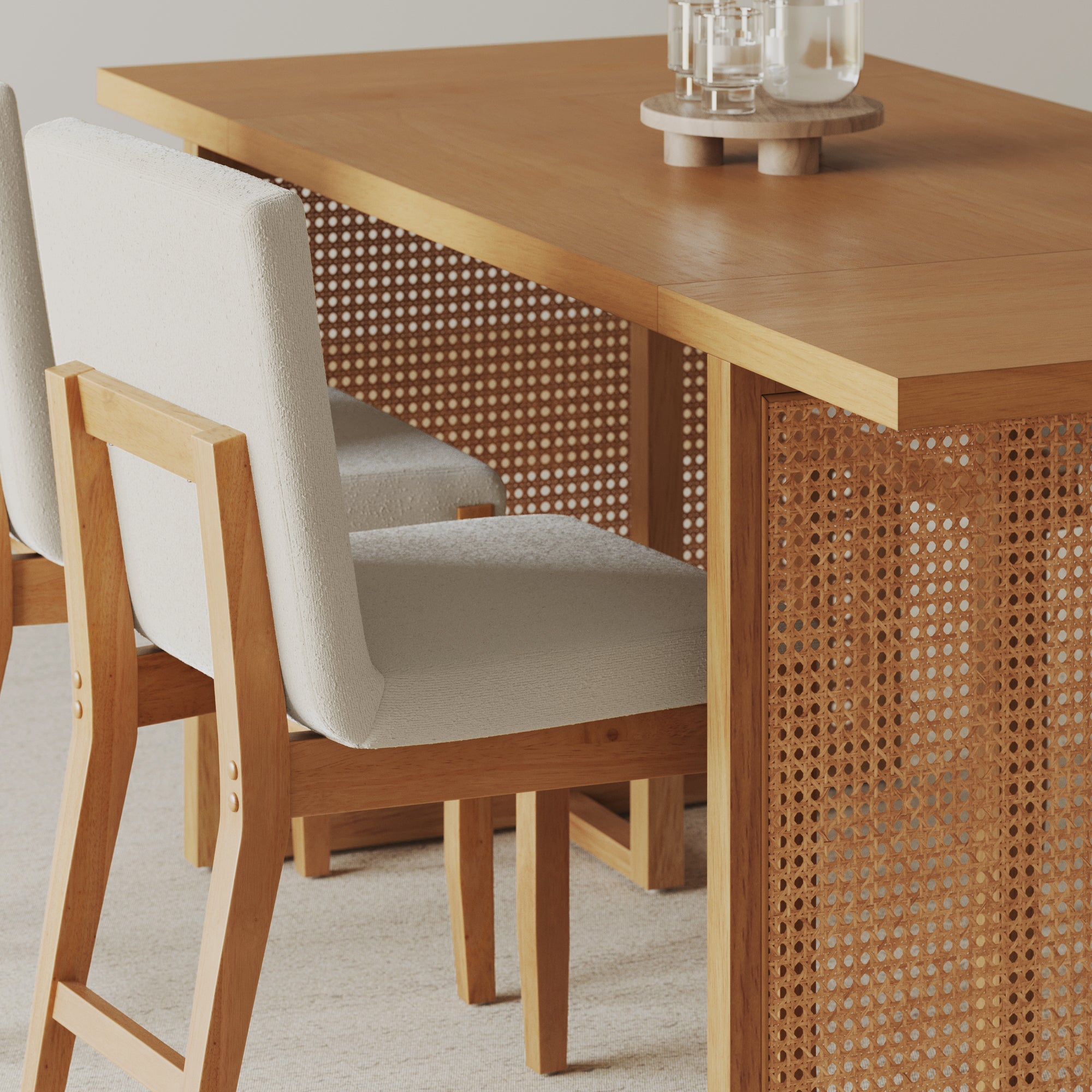 A wooden dining table with a woven cane panel and two cushioned chairs with light fabric seats and wooden frames, set on a neutral carpet. Glasses and a carafe are placed on the table.