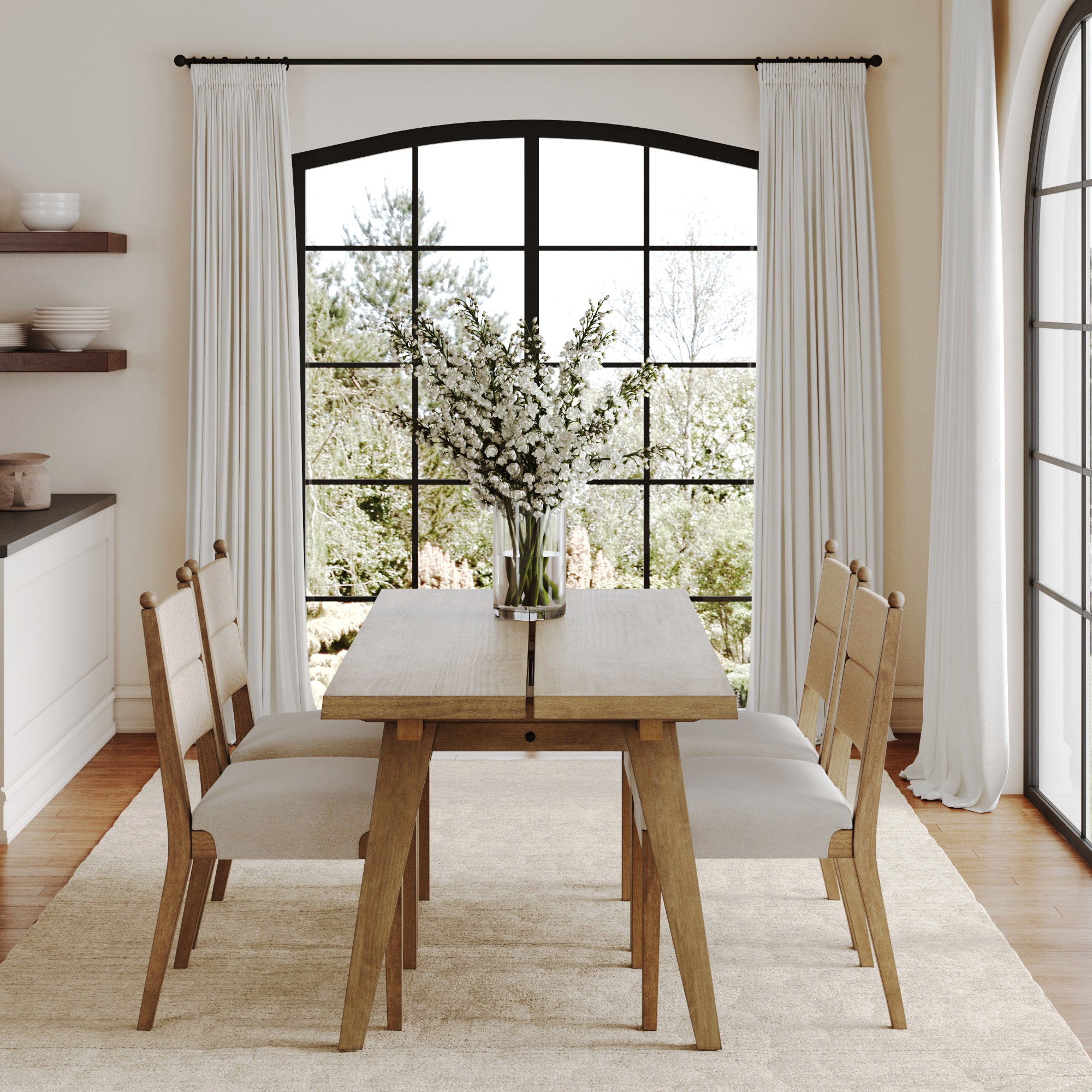 The Nathan James Boho Seagrass Dining Table Set, with four cushioned chairs and an oak veneer table, sits on a light rug by arched windows. A vase with white flowers accents the space, enhancing the natural light in the room.