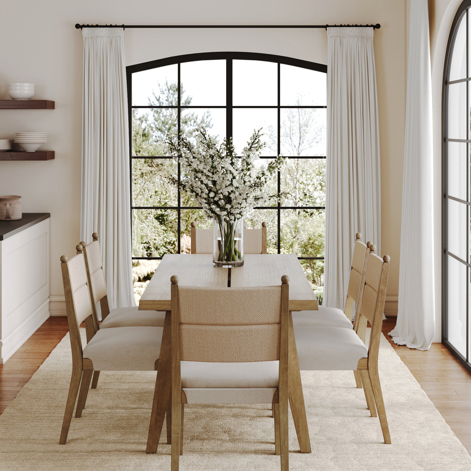 A dining room styled with the Nathan James Boho Seagrass Dining Table Set (6 Chairs), featuring an oak veneer table, seagrass chairs, a light rug, a vase with white flowers, black-framed windows, white curtains, and views of greenery.