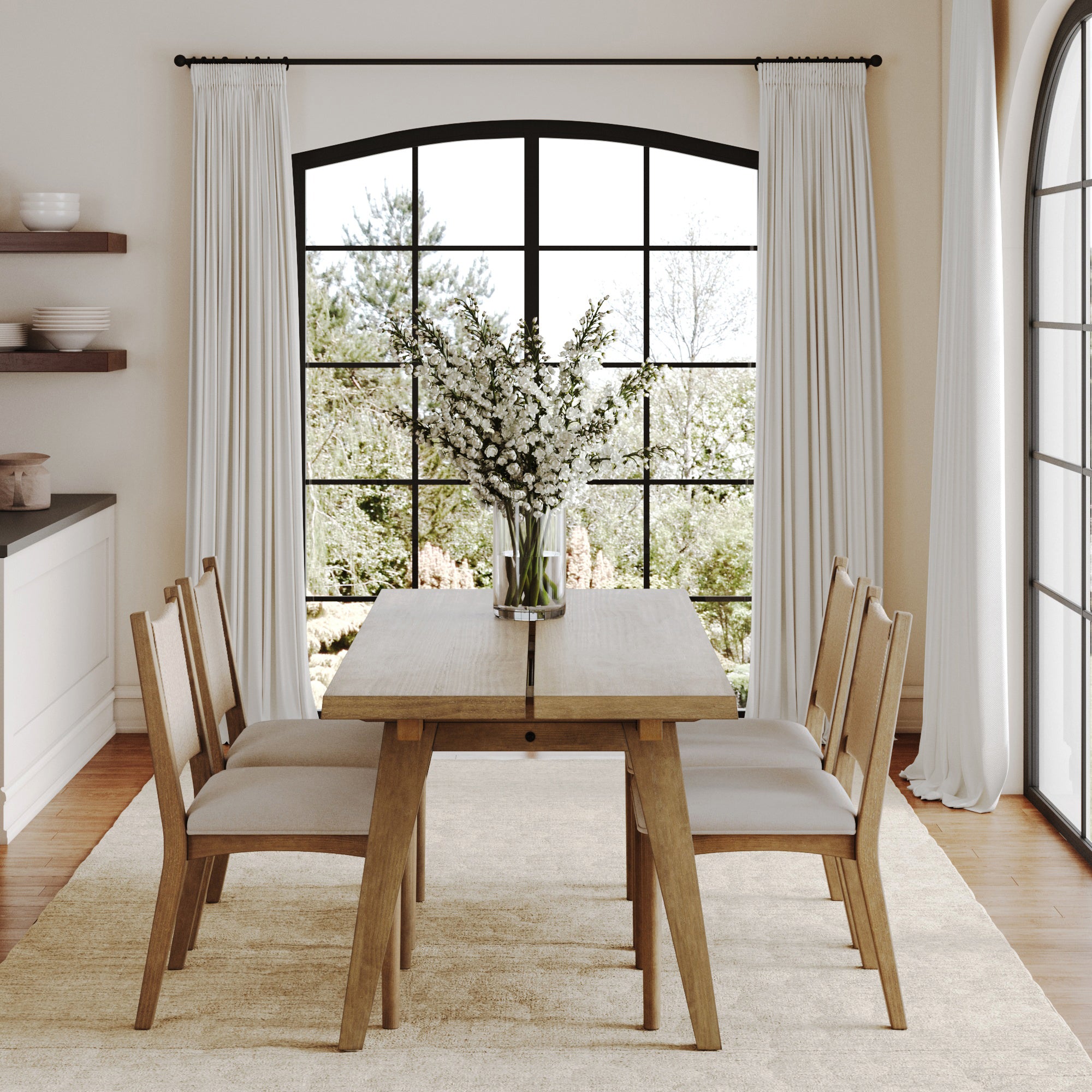 A modern dining room features the Nathan James Bohemian Wooden Dining Table Set with four matching chairs on a beige rug, a vase with white flowers on the table, and large windows with white curtains overlooking a garden.