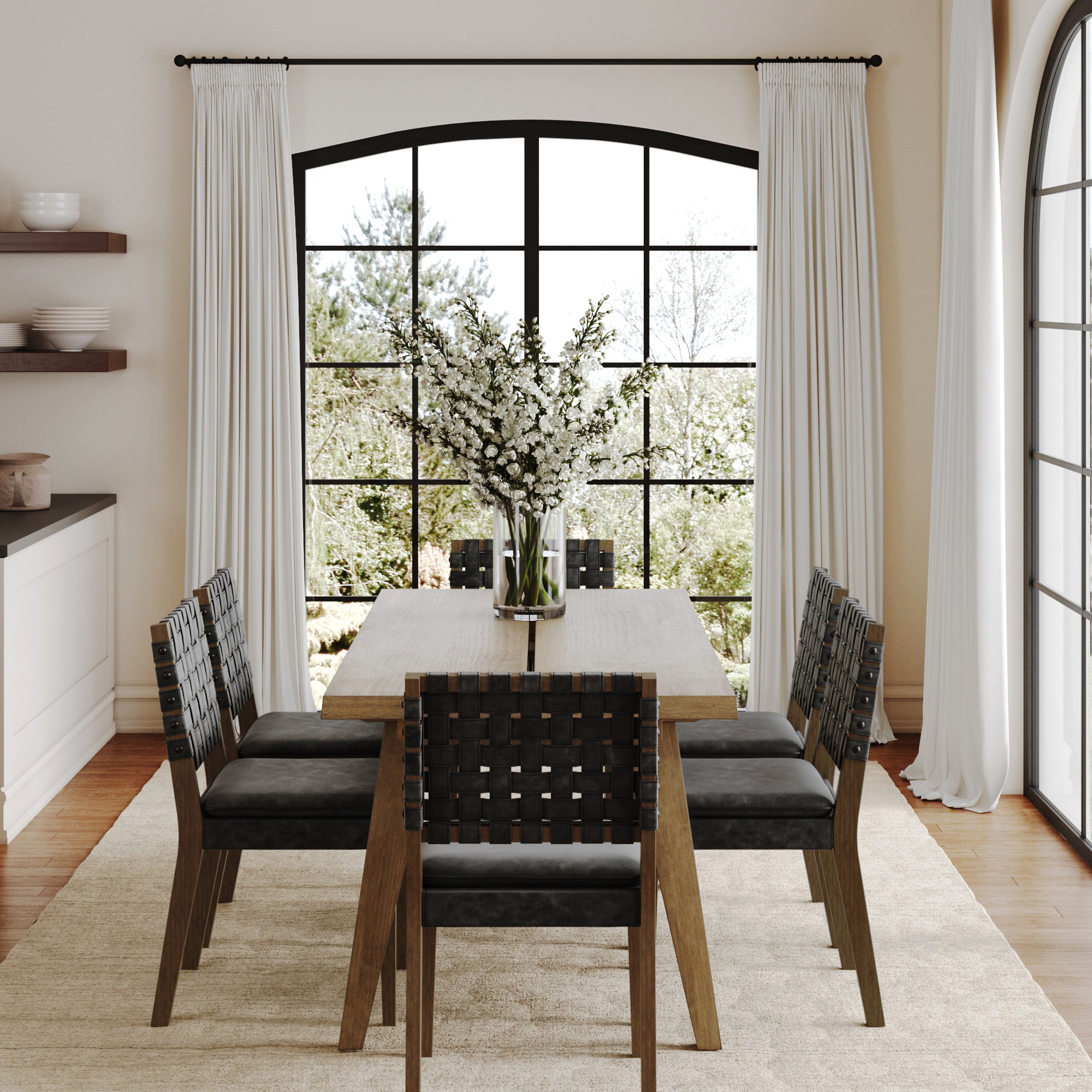 A modern dining room showcases the Nathan James Mid Century Faux Leather 6 Chairs Dining Set in black, a vase of white flowers, large black-framed windows with white curtains, a beige rug on hardwood floors, and views of trees outside.