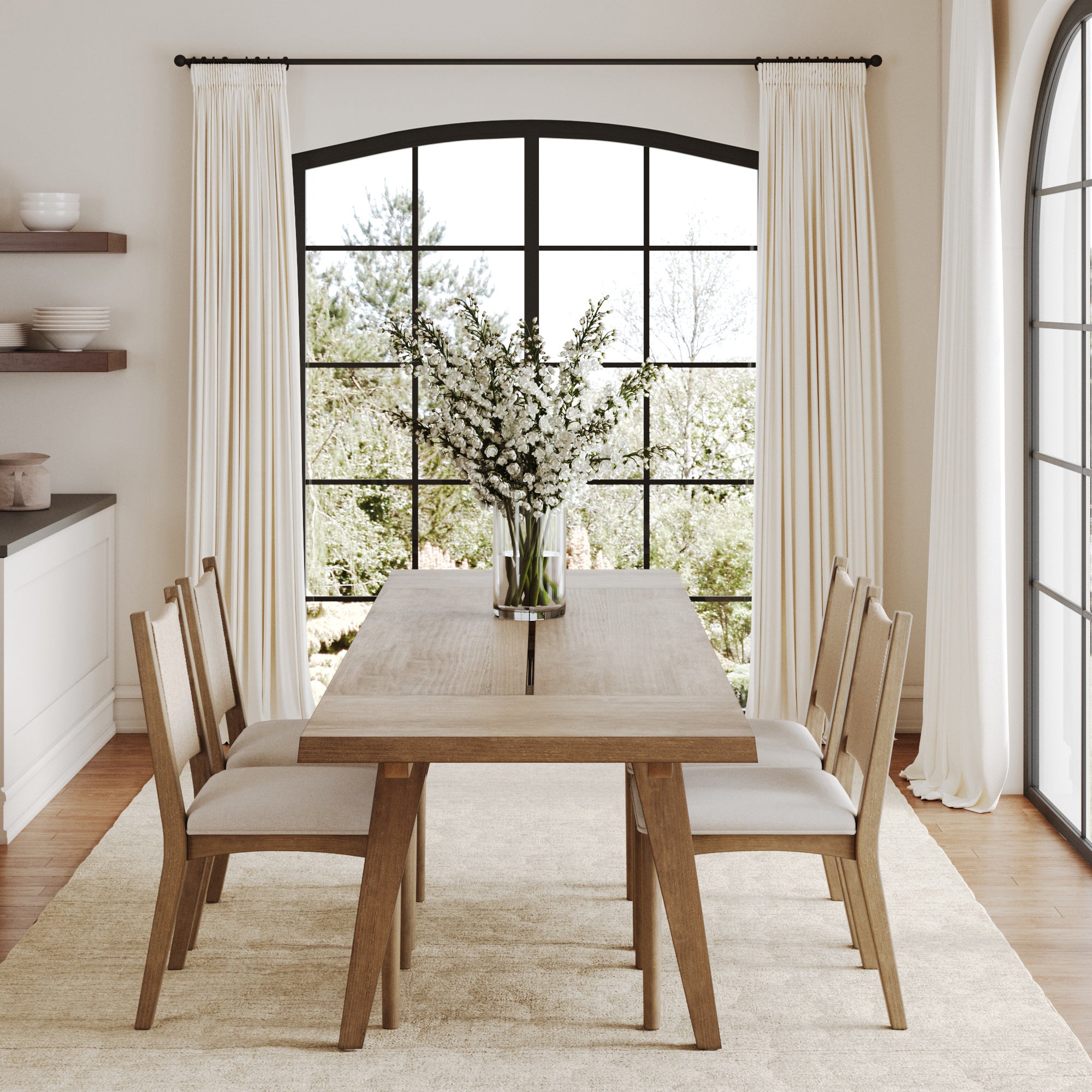 A modern dining room features the Nathan James Extendable Dining Table Set with 4 flax chairs, a vase of white flowers centerpiece, cream curtains on large windows, a beige rug on wooden floors, and greenery visible outside.