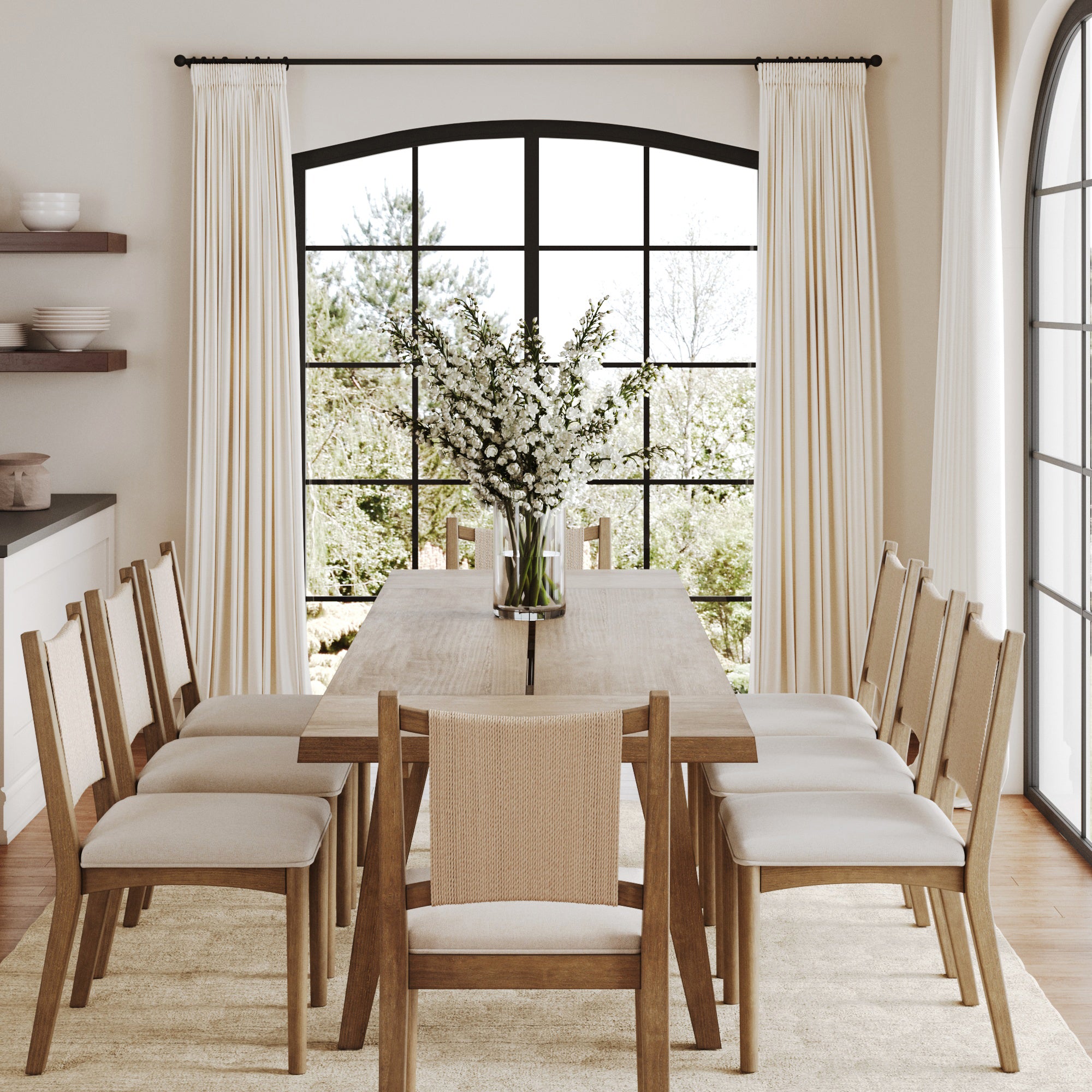 A modern dining room with a Nathan James Bohemian Wooden Dining Table Set (8 Chairs), a vase of white flowers, black-framed windows, cream curtains, and soft natural light.