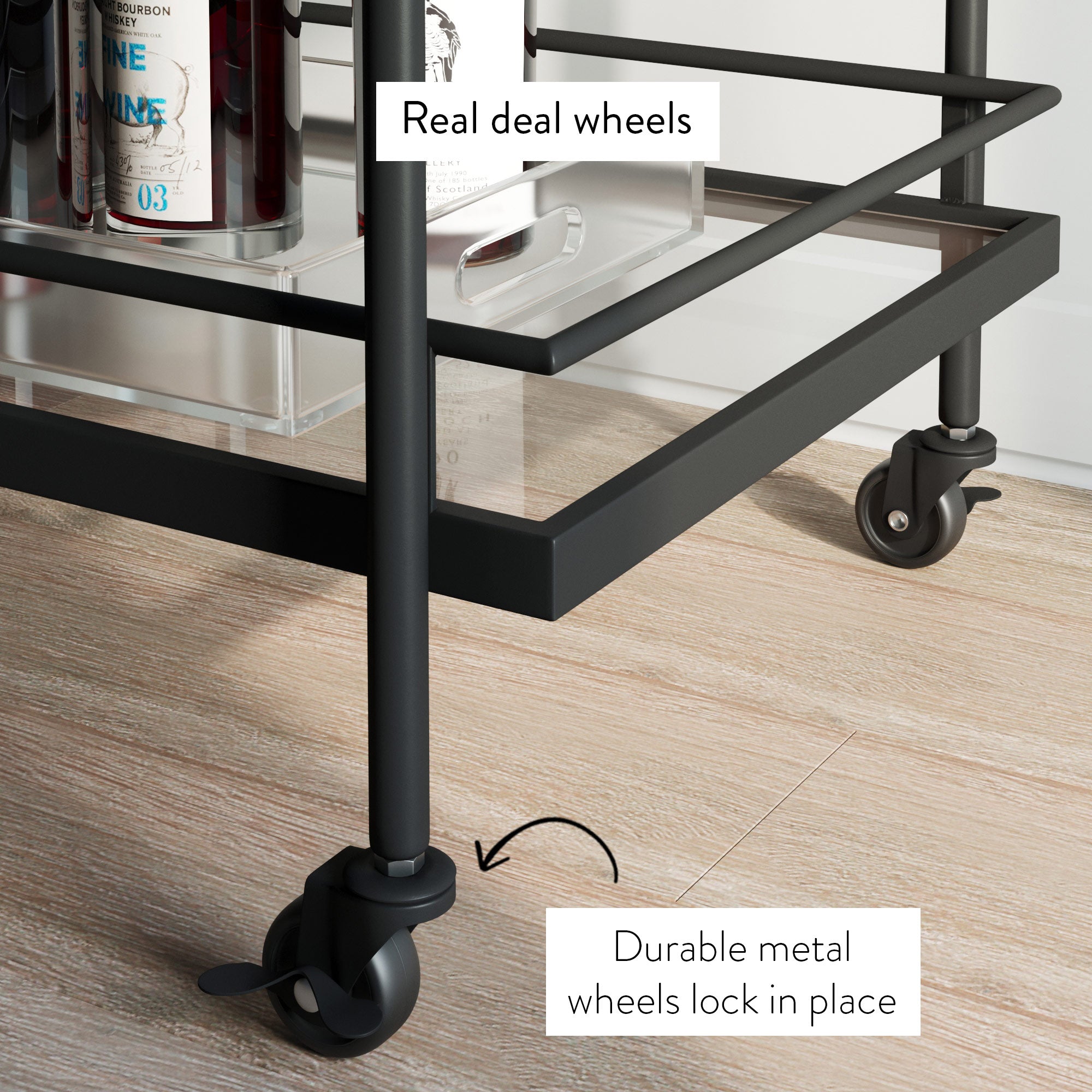 Close-up of a black metal bar cart on wood flooring, focusing on its locking caster wheels. Labels point to the wheels, highlighting that they are real and made of durable metal, which lock in place. Bottles are visible on the shelf above.