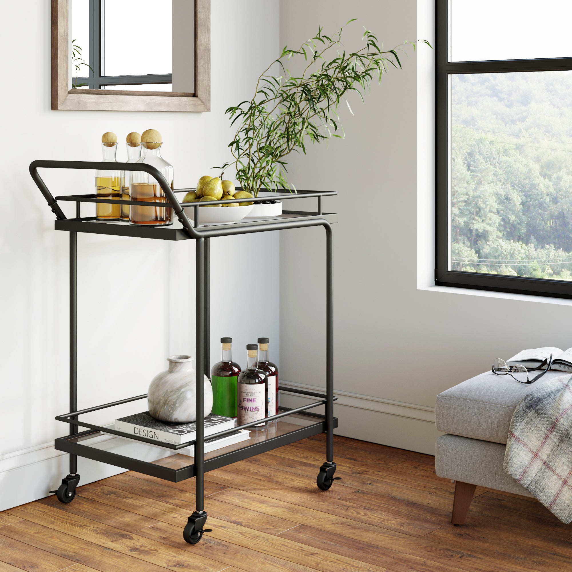 A black metal bar cart with two shelves holds bottles, a tray with lemons, and a plant. It stands on wooden floors near a window and a light gray ottoman with a plaid blanket. A mirror hangs on the wall above the cart.
