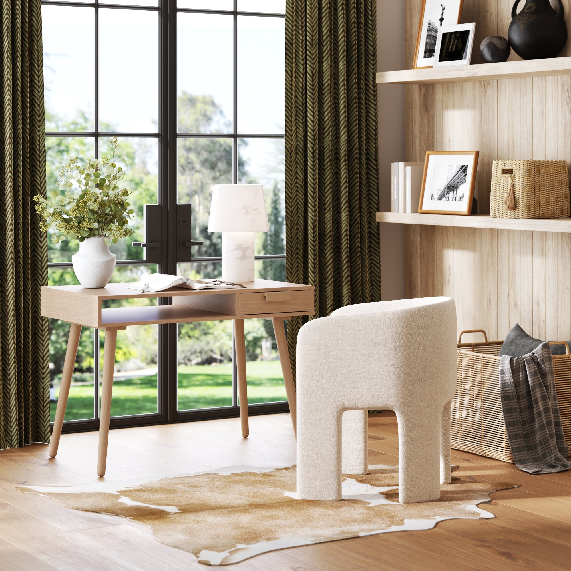 A modern home office featuring the Nathan James Wood Mid-Century Modern Desk with Drawer in Raw Oak, a white chair, lamp, vase with flowers, cowhide rug, built-in shelves with decor accents, and large windows overlooking greenery.