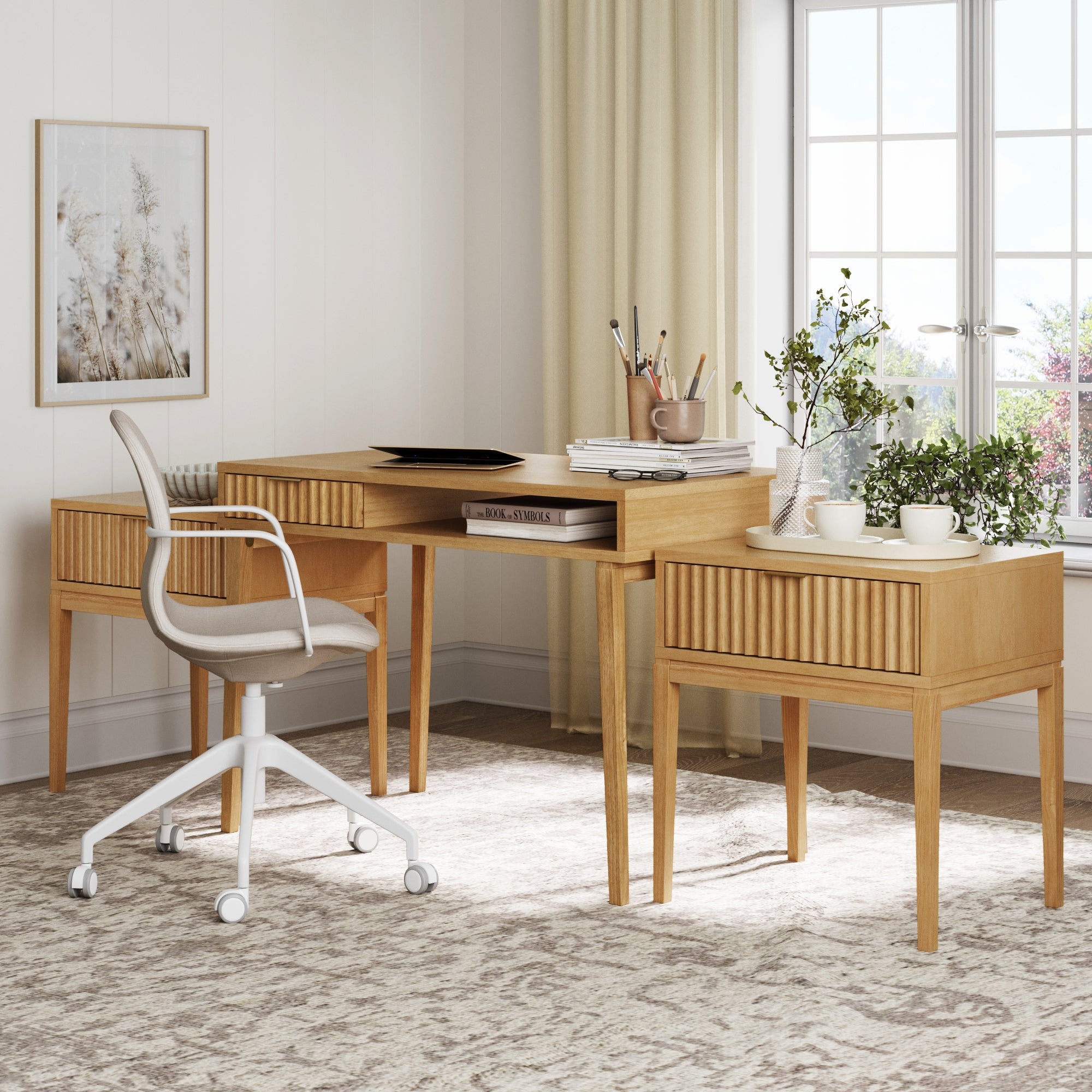A modern home office showcases the Nathan James Solid Wood Fluted Desk & 2 Nightstands Bedroom Vanity Set, paired with a white cushioned swivel chair, potted plants, books, art supplies, and decor. Natural light fills the space through large windows with beige curtains.