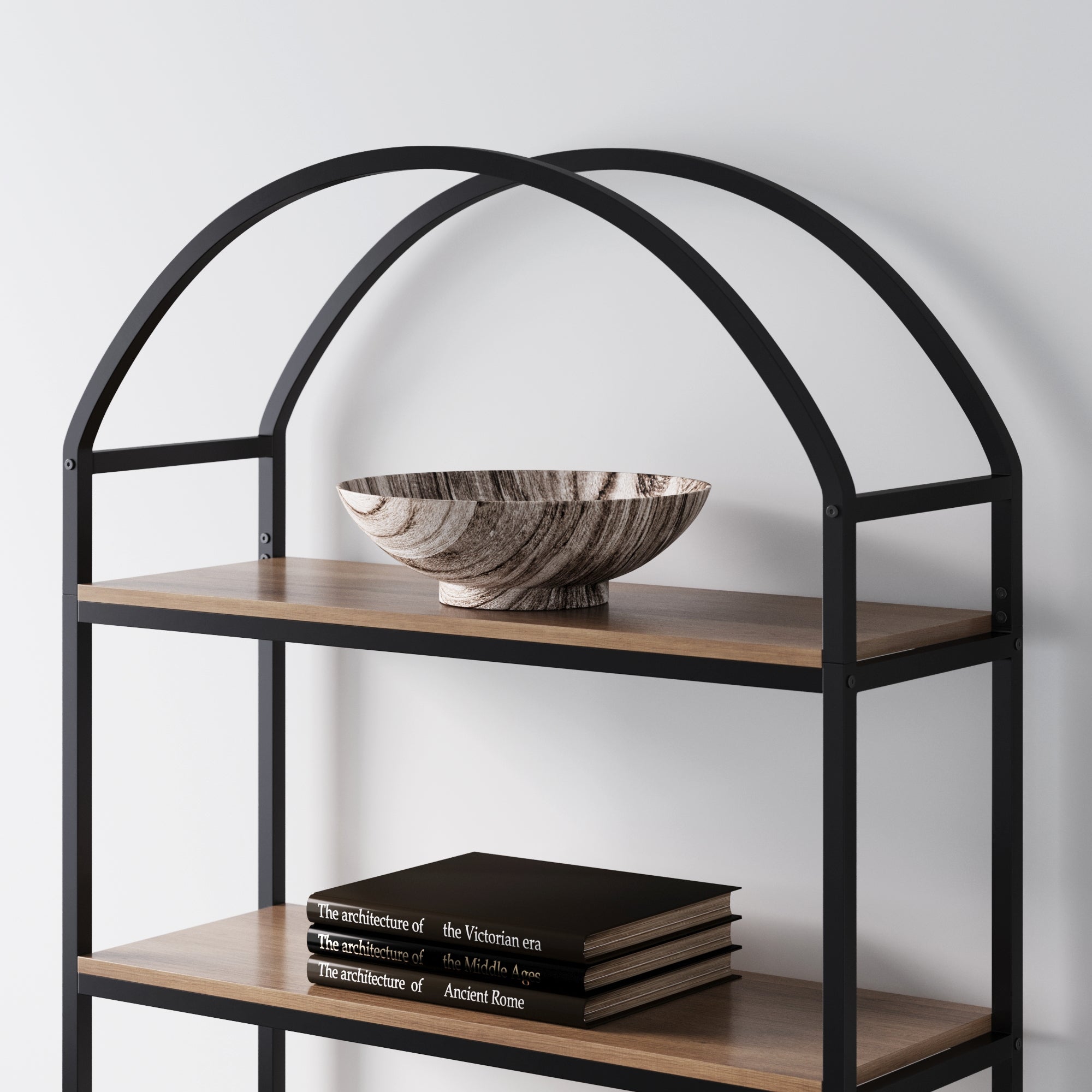 A modern black metal and wood bookshelf holds a decorative marbled bowl on the top shelf and three black hardcover books stacked on the lower shelf against a white wall.
