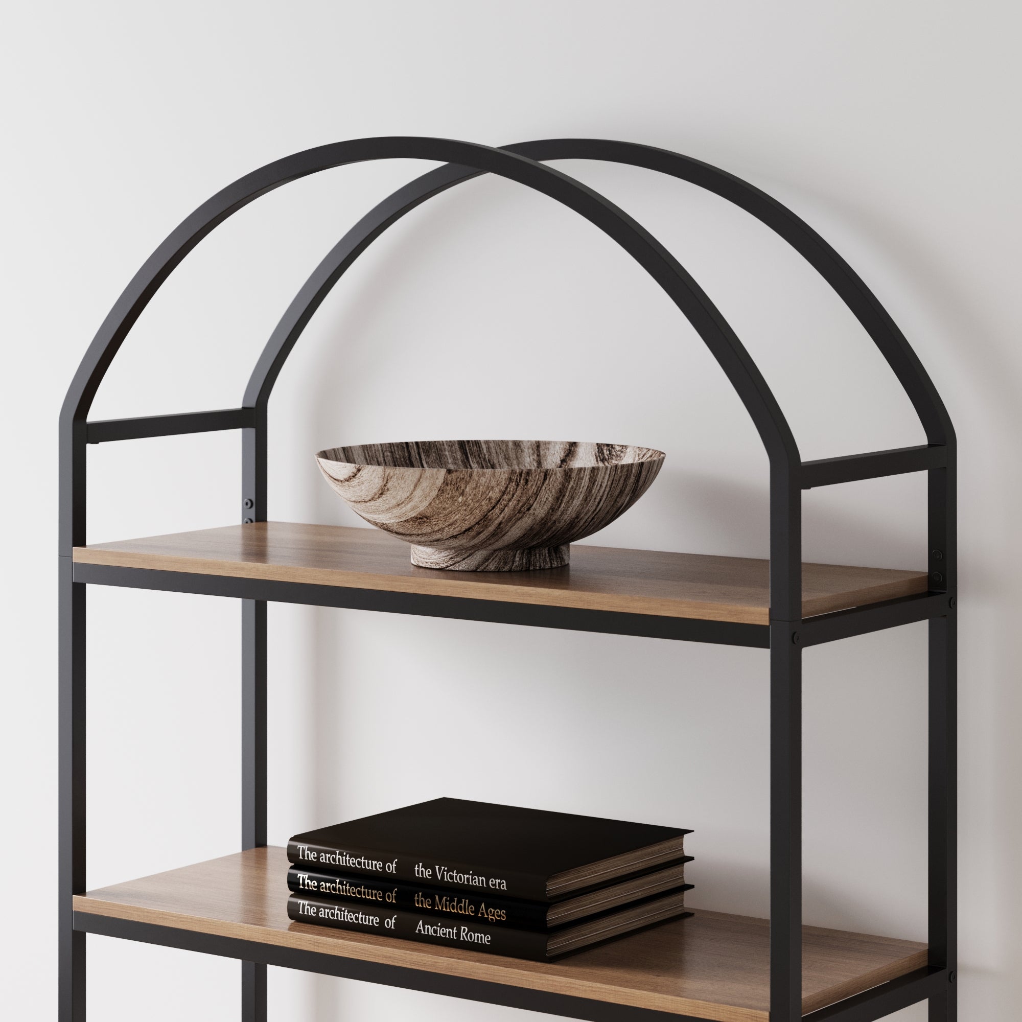 A modern metal and wood bookshelf with an arched frame, featuring a wood-patterned bowl on the top shelf and three stacked black books with white titles on the shelf below.