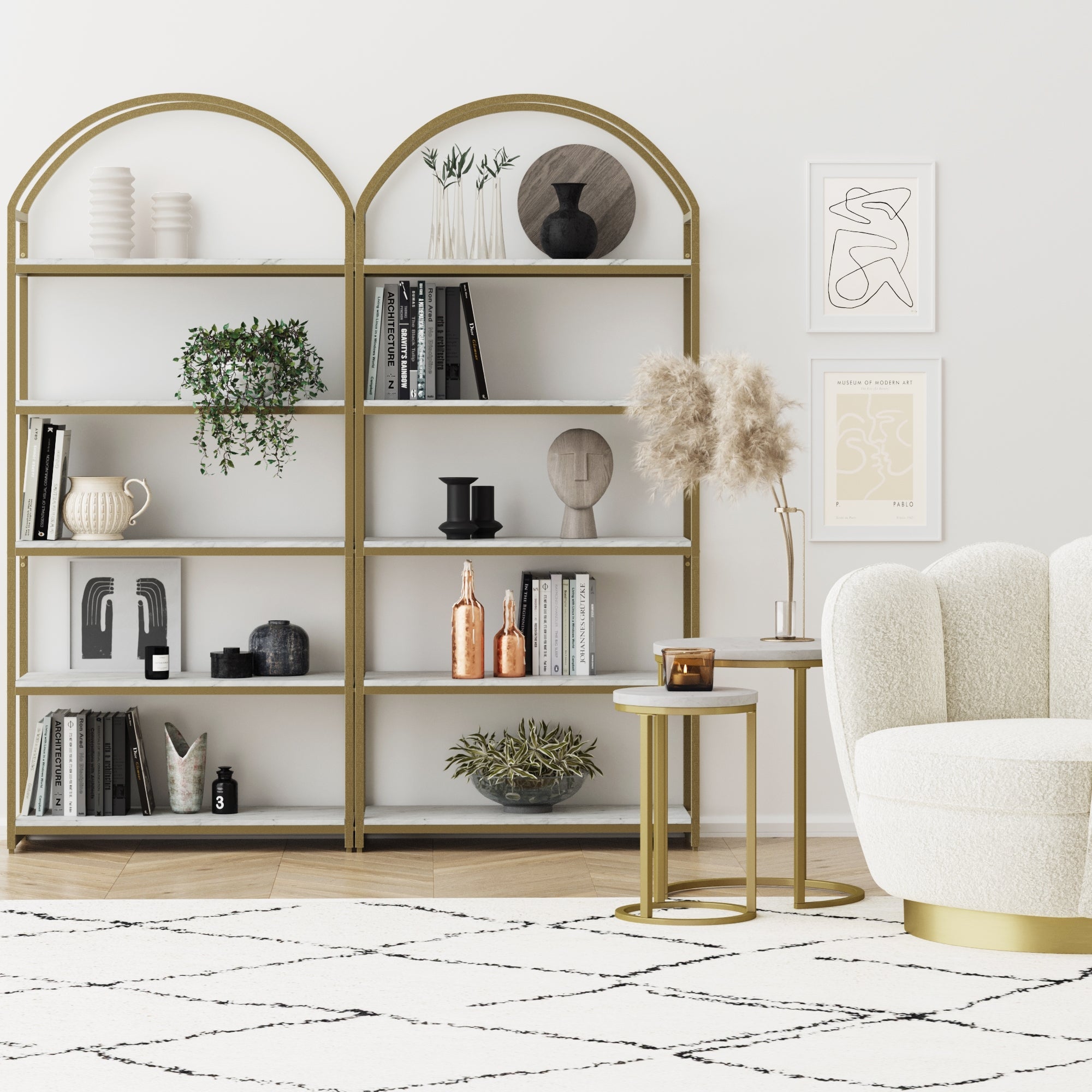 Modern living room featuring Nathan James Metal 5-Shelf Arched Bookshelves Gold (Set of 2) displaying books, plants, and vases; abstract art; round side tables with pampas grass; and a cream armchair on a patterned rug.