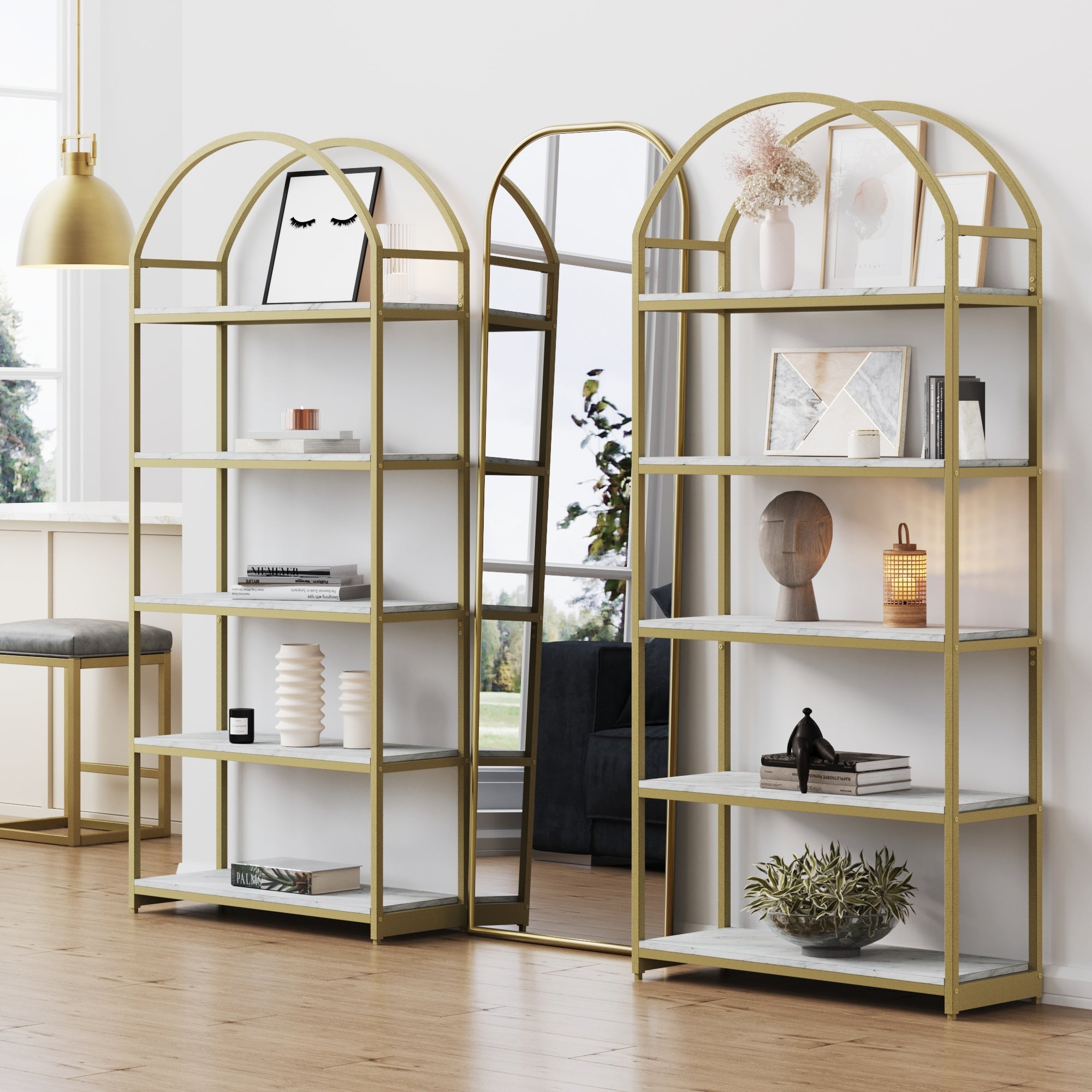 The Nathan James Metal 5-Shelf Arched Bookshelves Gold (Set of 2) stand side by side, displaying books, vases, art, and plants in a modern room with wood floors and large windows for a chic etagere style.