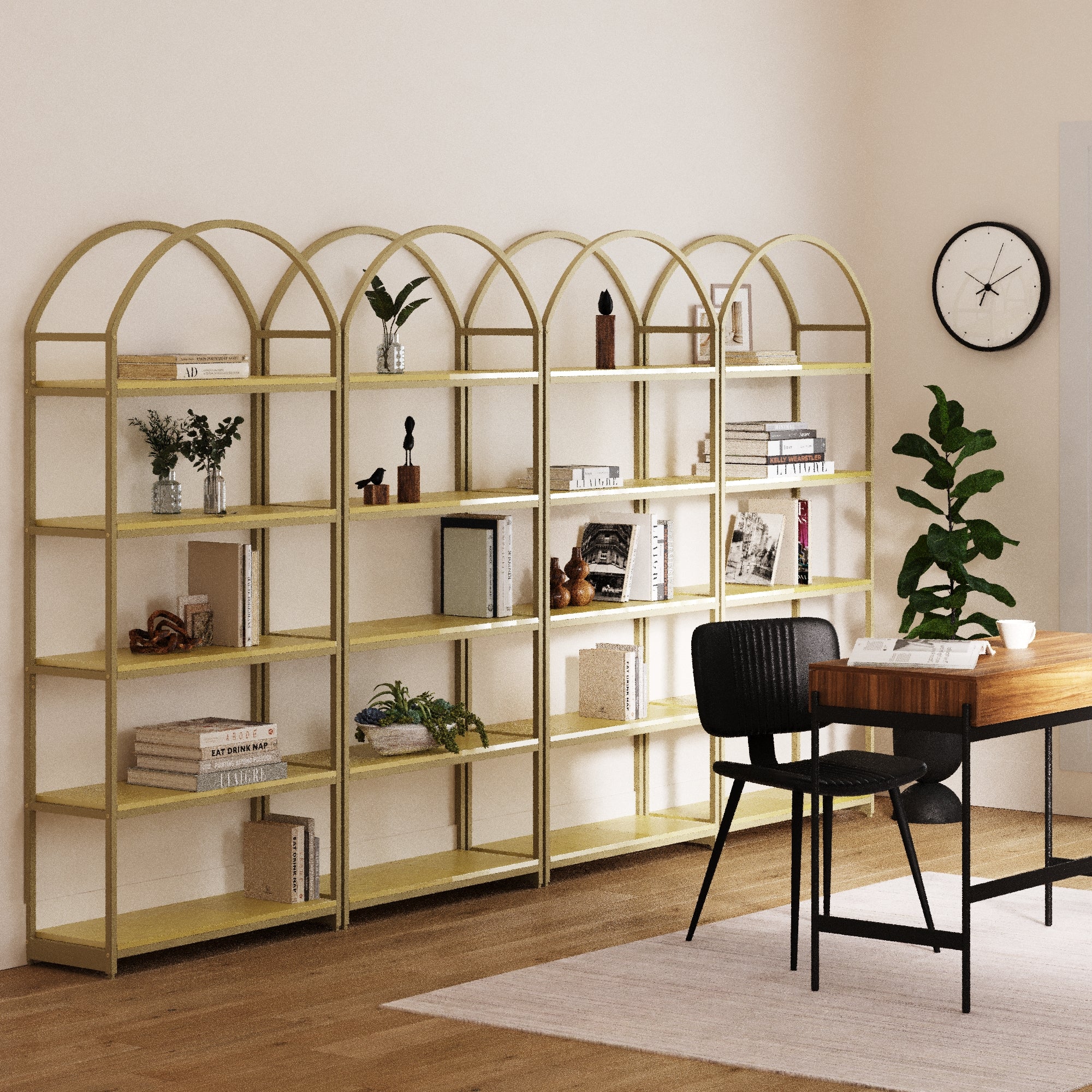 A modern room features four Nathan James Metal 5-Shelf Arched Bookshelves in gold, displaying books, plants, and decor. A wooden desk with a black chair sits on a rug. There’s a wall clock, potted plant, light wood floor, and cream walls.