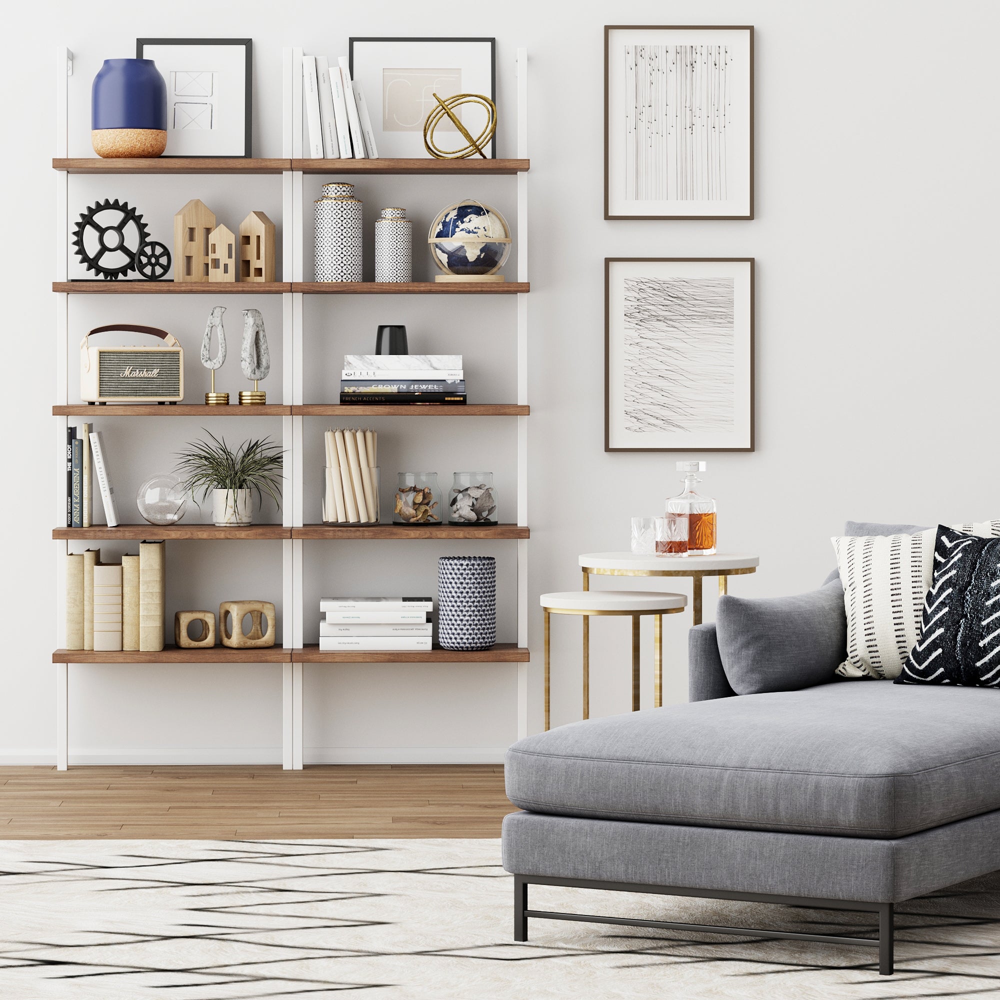 Modern living room with a gray sectional sofa, patterned cushions, a geometric rug, and a wooden bookshelf filled with art, books, decor pieces, and plants, against a white wall with framed artwork.