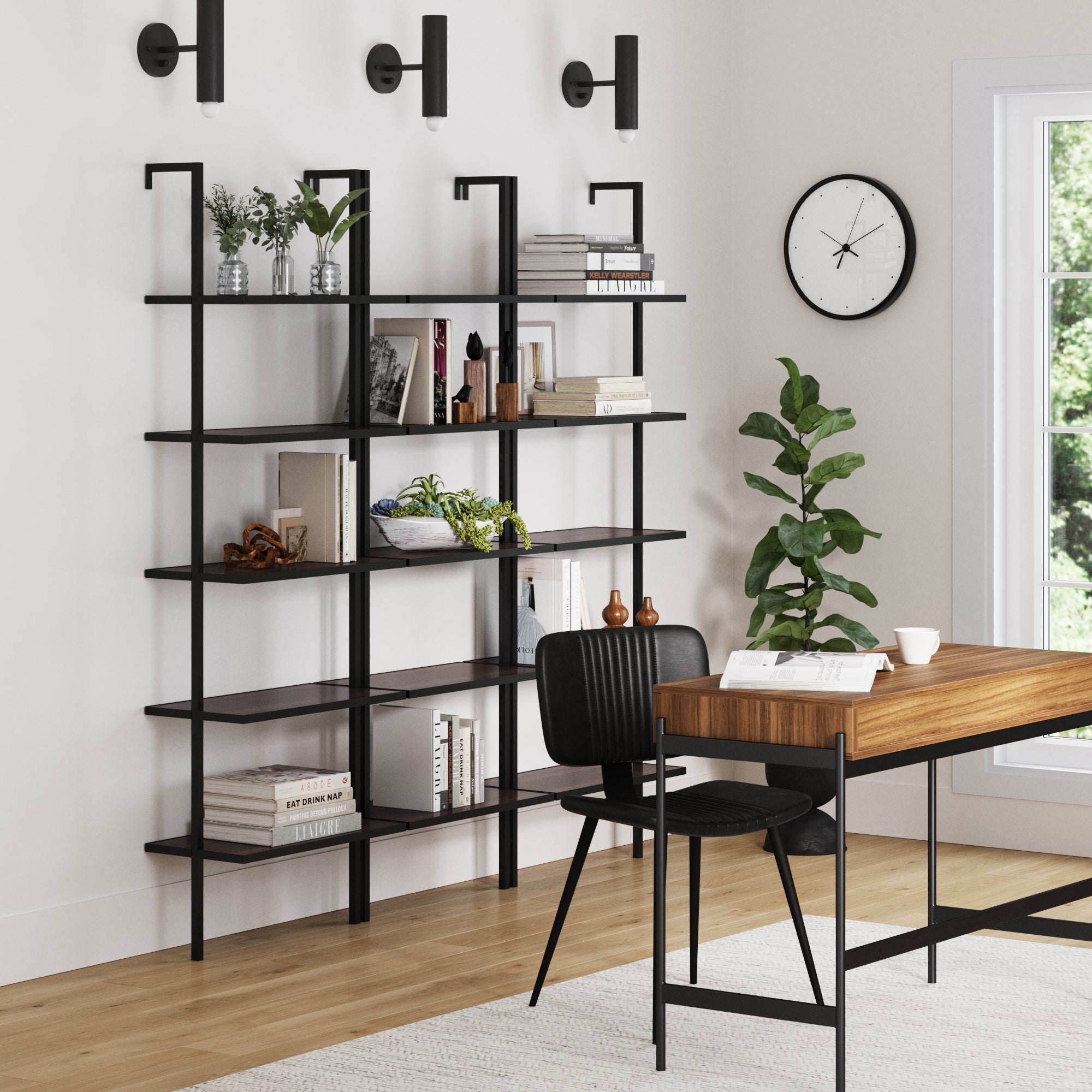 Modern home office with three Nathan James 5-Shelf Bookshelf Walnut Matte Black units showcasing books, plants, and decor, paired with a wooden desk, black chair, wall clock, potted plant, and a large window bringing in natural light.