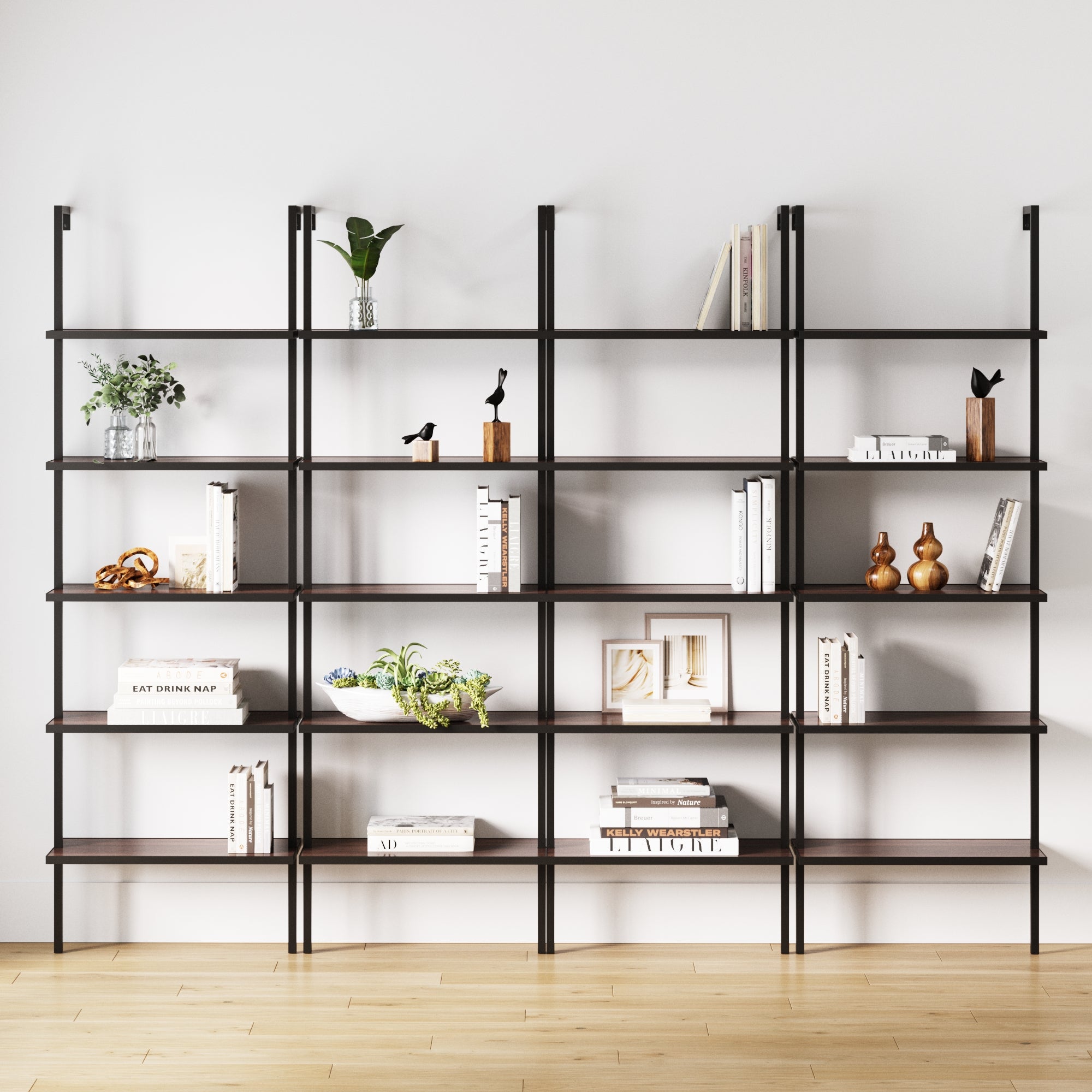 The Nathan James 5-Shelf Bookshelf Walnut Matte Black (Set of 4) is wall-mounted against a white wall and wood floor, elegantly styled with books, potted plants, vases, and minimalistic sculptures.