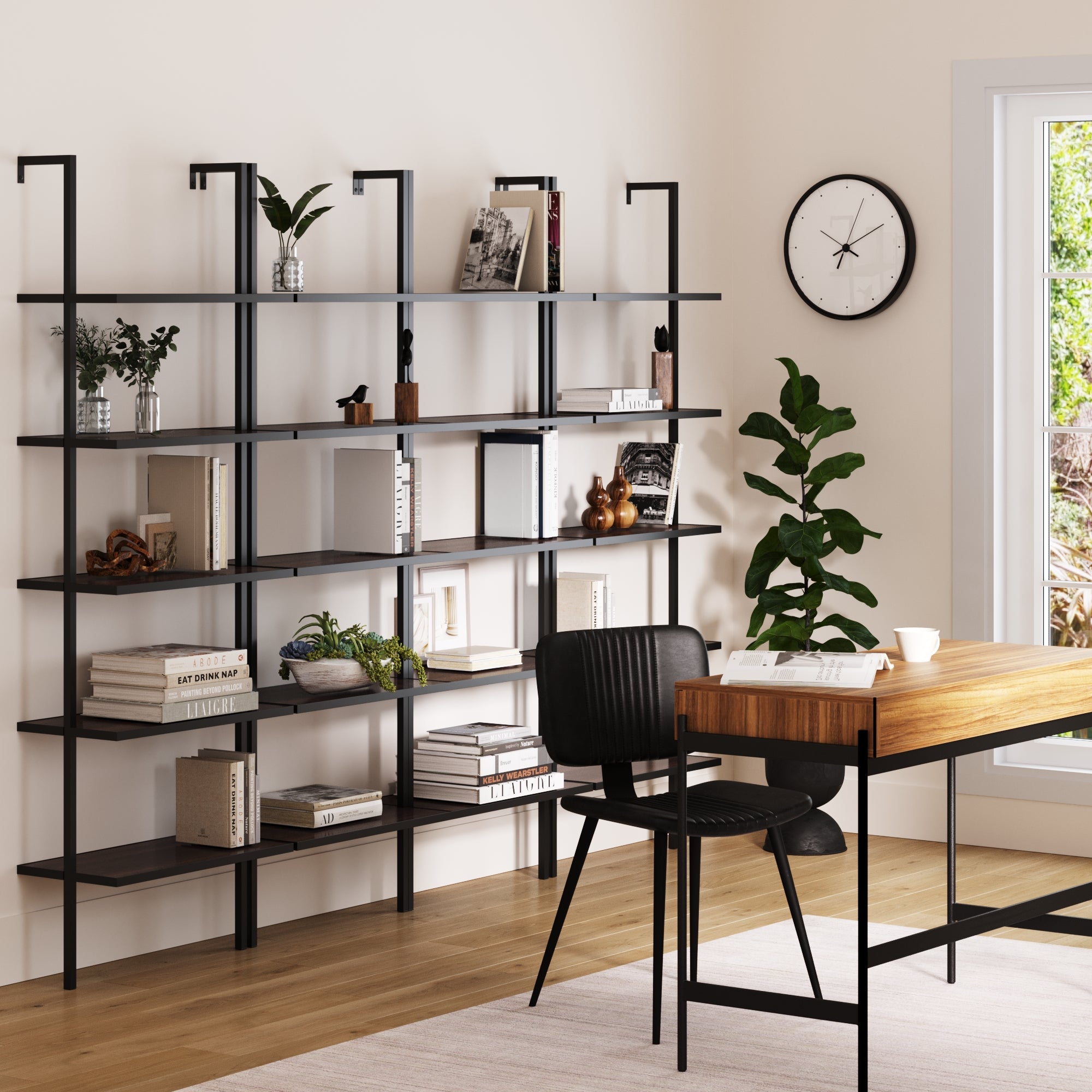 A modern home office with a wooden desk, black chair, Nathan James 5-Shelf Bookshelf Walnut Matte Black (Set of 4) filled with books and decor, a potted plant, wall clock, and a bright window letting in natural light.