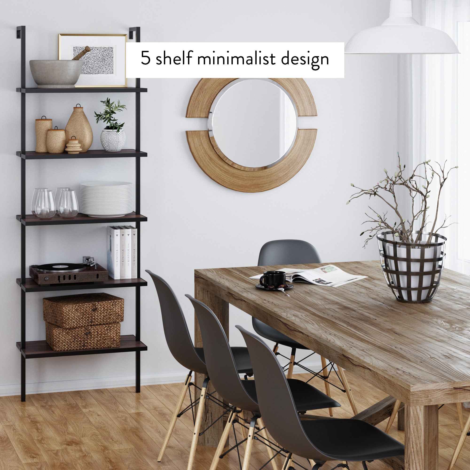 A modern dining room with a wooden table, black chairs, a round wall mirror, and a 5-shelf minimalist black shelving unit displaying decor items, books, and baskets. A large plant sits on the table.