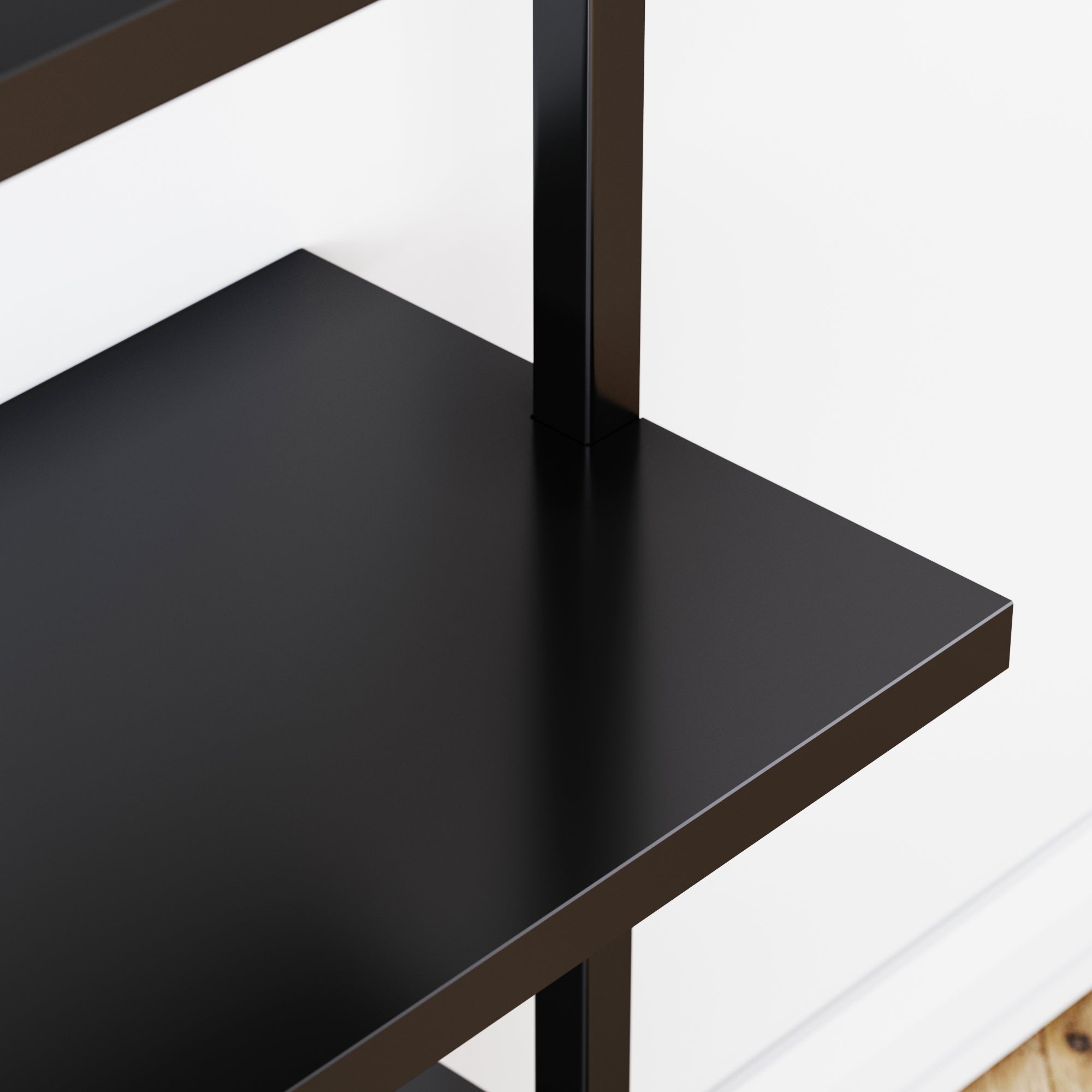 Close-up view of a sleek, black metal shelf with a modern design, positioned against a white wall and near a light wood floor.