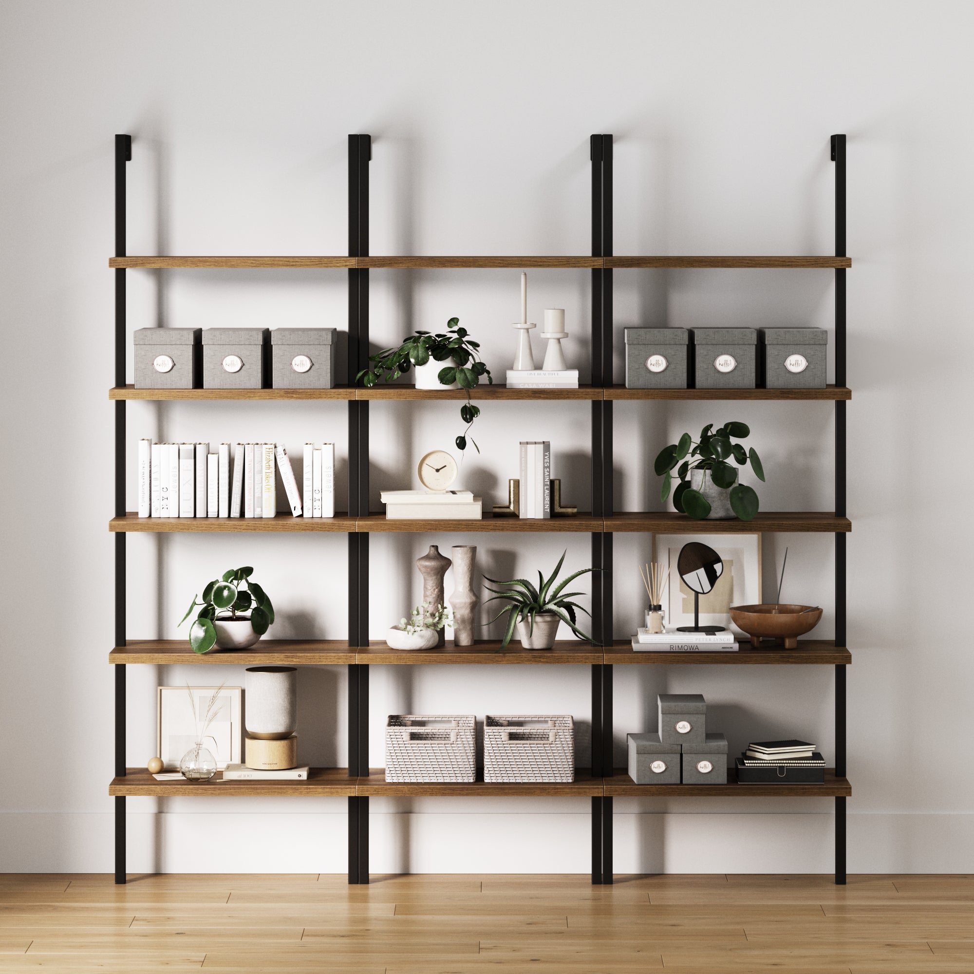 The Nathan James 5-Shelf Ladder Bookshelf Oak Matte Black (Set of 3) combines wood and metal to neatly display books, decor, plants, baskets, and storage boxes against a white wall on a light wood floor.