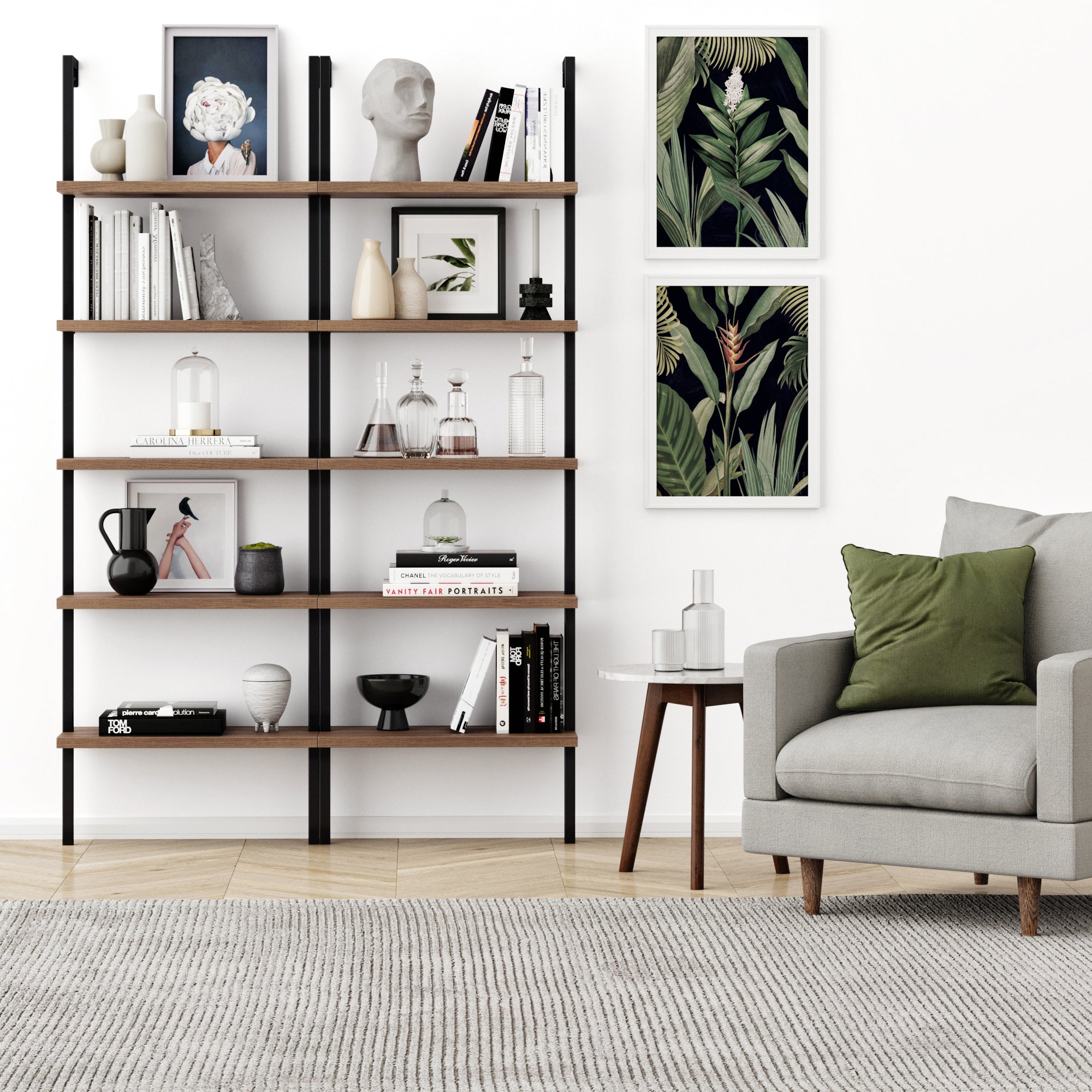 A modern living room with a gray armchair, green pillow, wooden side table, a Nathan James 5-Shelf Ladder Bookshelf in Oak Matte Black with decor and books, two framed botanical prints on a white wall, and a light rug on wood floors.