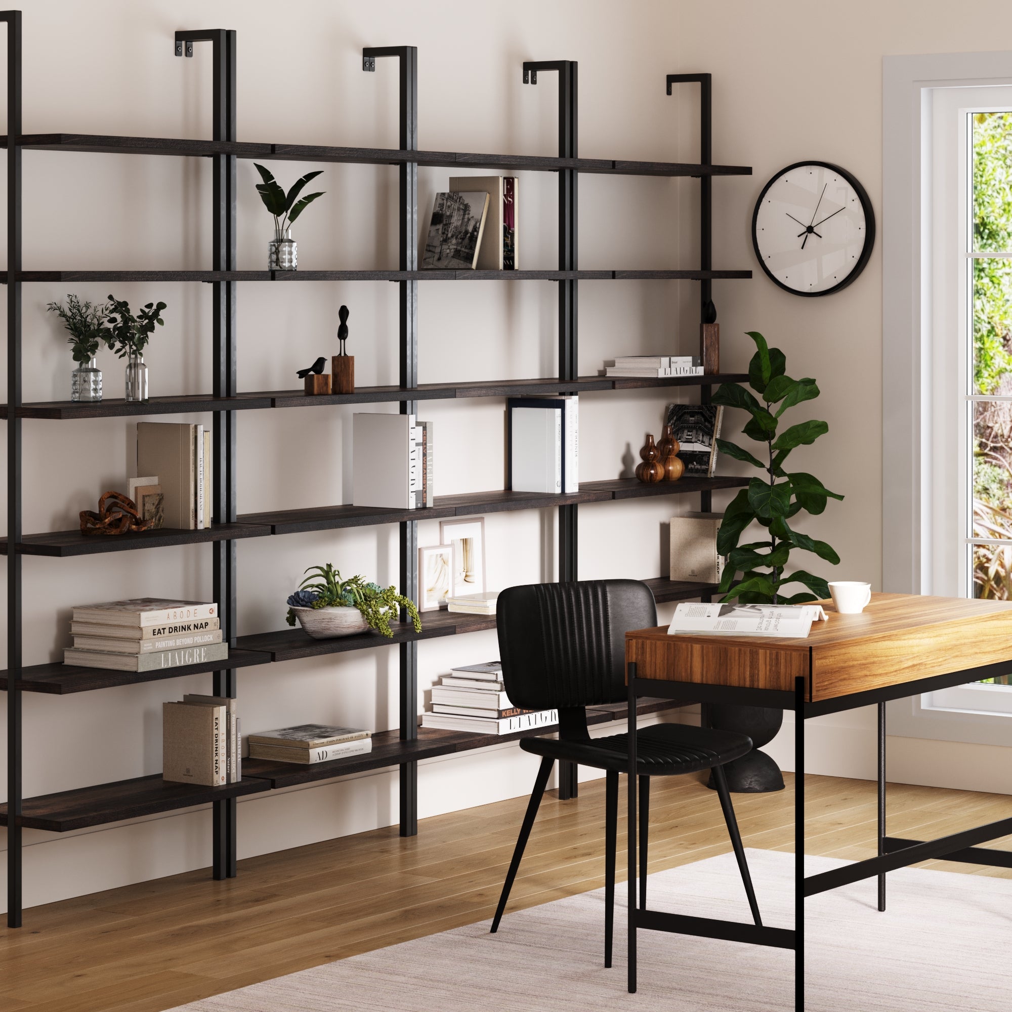A modern home office with a wooden desk, black chair, clock, large window, and Nathan James 6-Shelf Bookcase Nutmeg Matte Black (Set of 4) displaying books, plants, and decor.