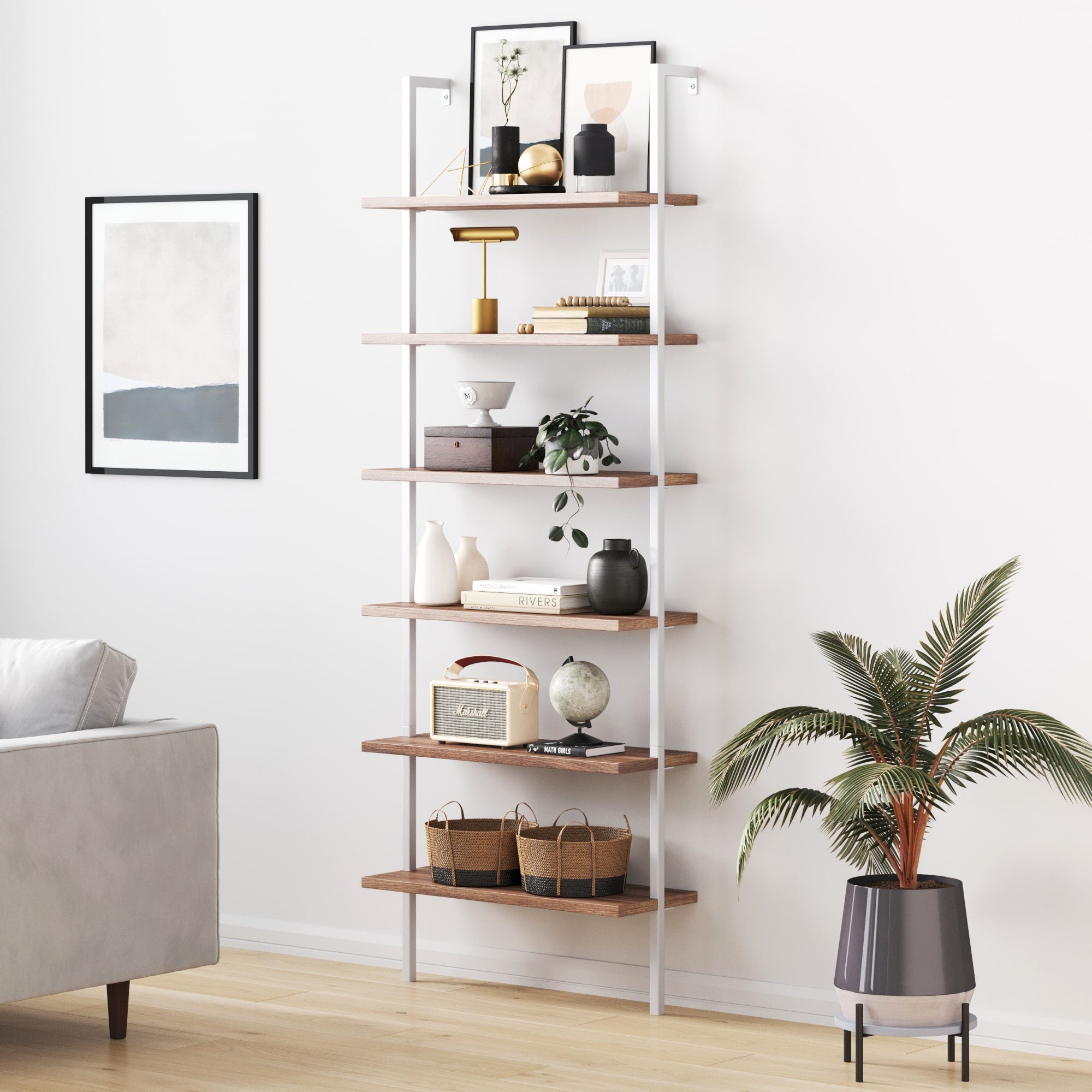 A modern, tall shelving unit with wooden shelves and white frame, decorated with books, vases, art pieces, plants, and baskets. It stands against a white wall near framed artwork, a gray sofa, and a potted plant.
