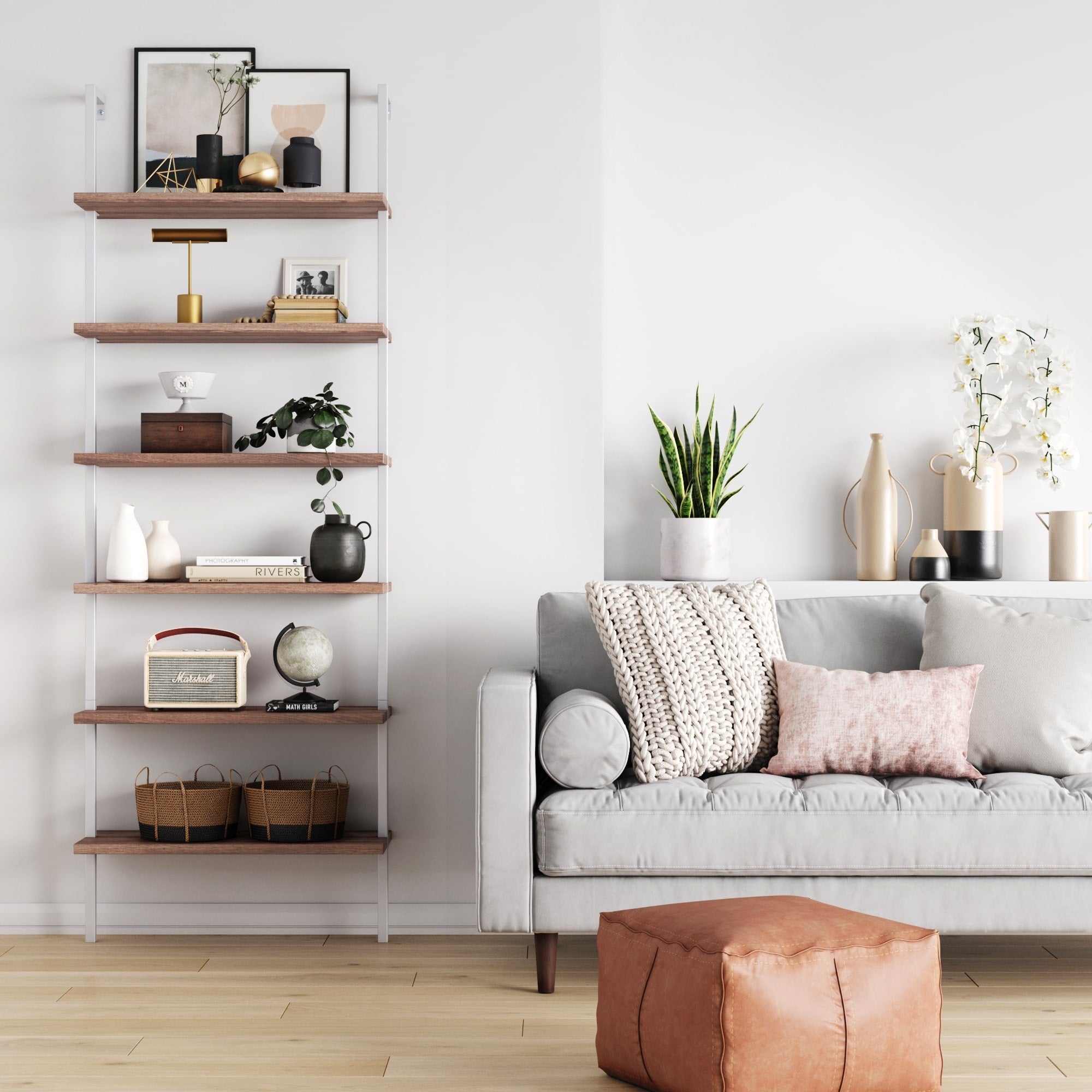 A modern living room featuring a gray sofa, pink and cream cushions, brown ottoman, white console table with plants and decor, and the Nathan James 6-Shelf Ladder Bookshelf Oak Matte White displaying books and accents against a white wall.