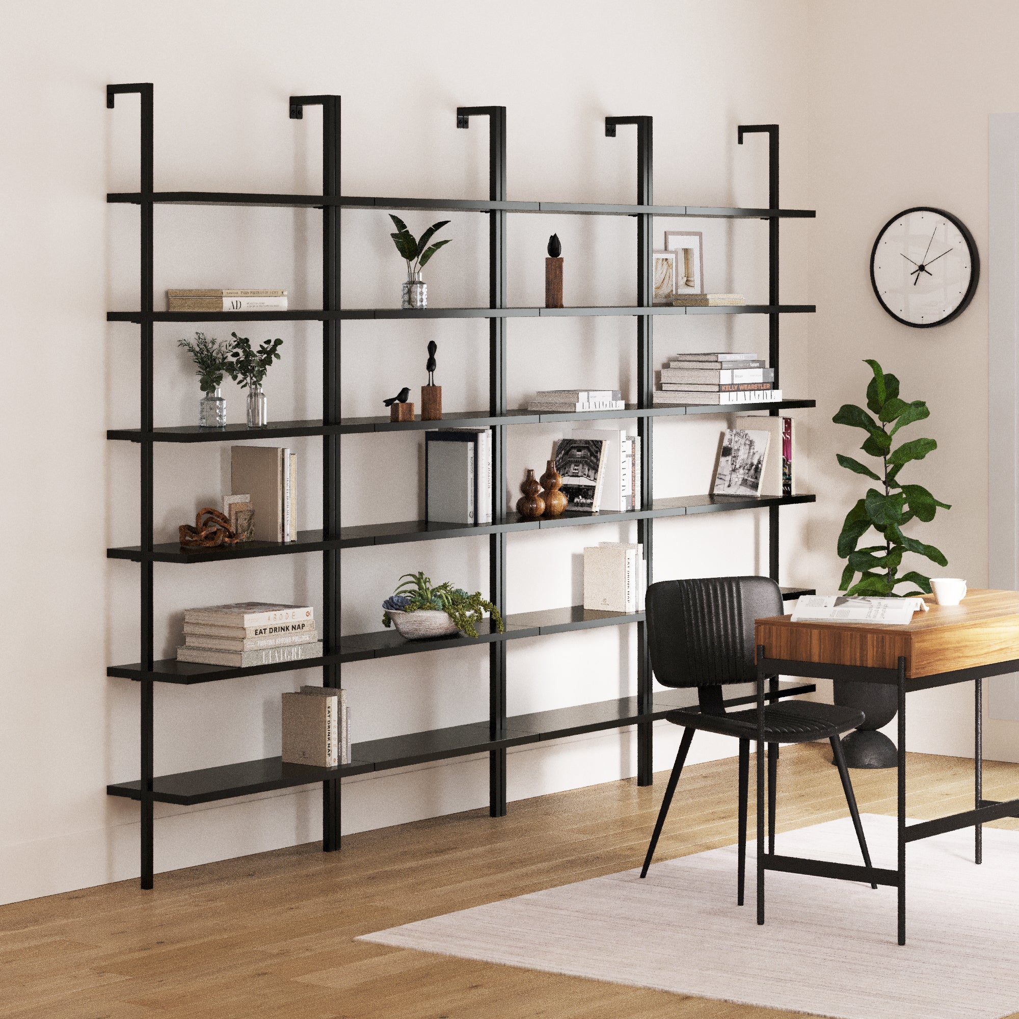 A modern home office showcases four Nathan James 6-Shelf Wall Mount Bookshelves in black, filled with books, plants, and decor. A wooden desk with a black chair faces them, while a wall clock and potted plant add charm.