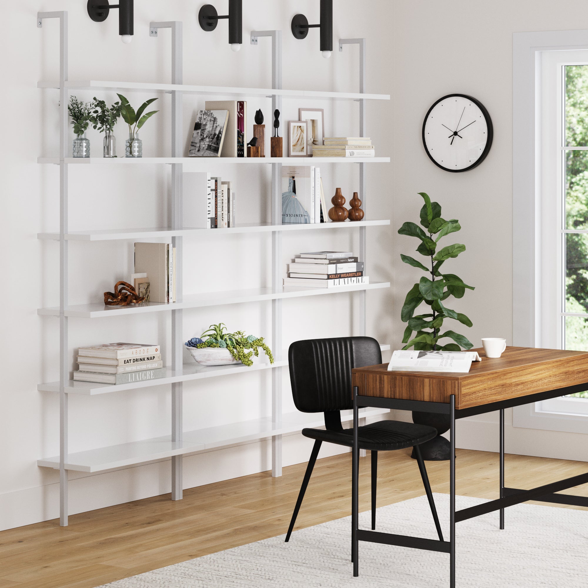 A modern office with a wooden desk, black chair, wall clock, large window, and three Nathan James 6-Shelf Ladder Bookshelves in white filled with books, plants, and decor against a crisp white wall.
