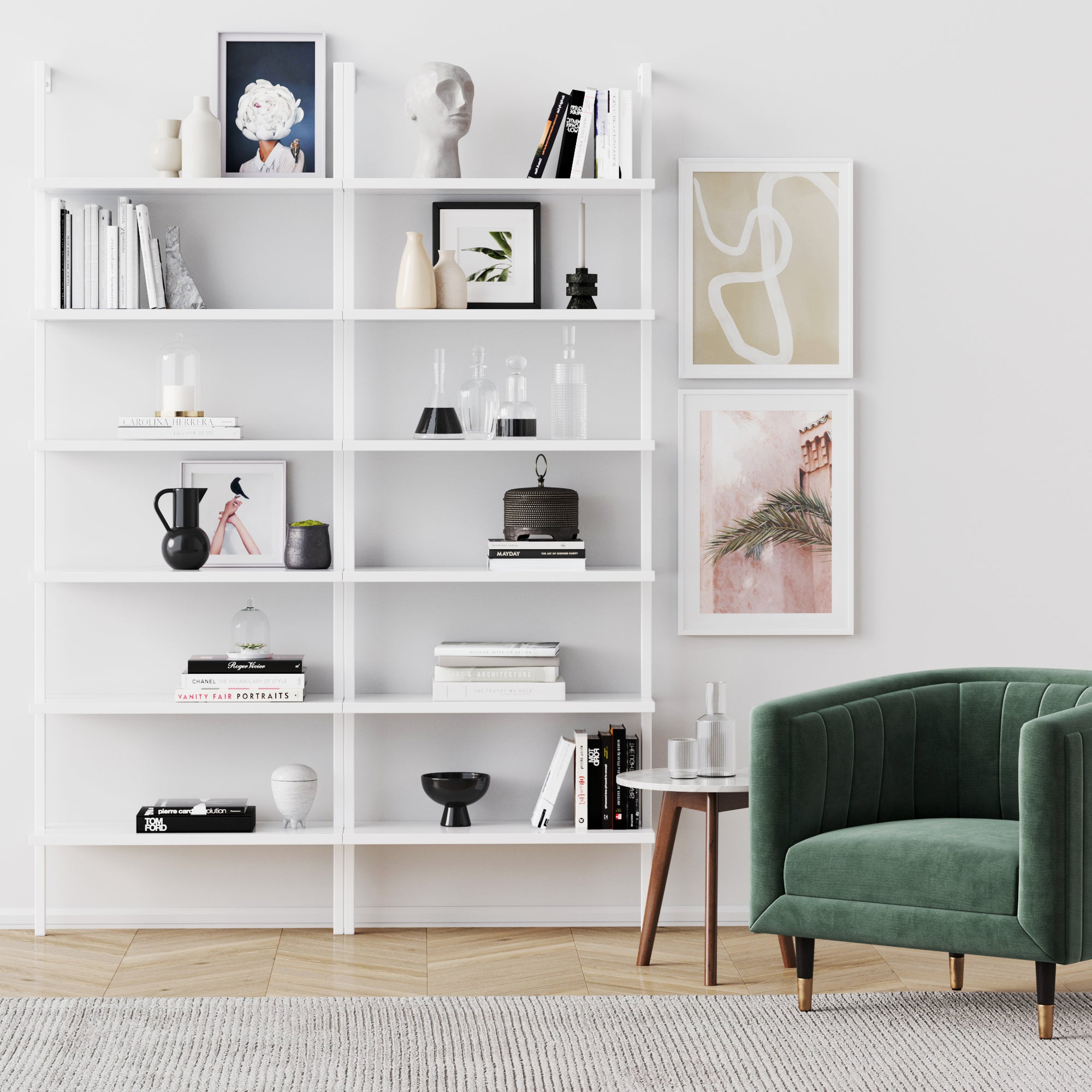 A modern living room showcases the Nathan James 6-Shelf Ladder Bookshelf in white, filled with books, vases, and art. Three framed pictures hang above a green velvet armchair beside a small round table.