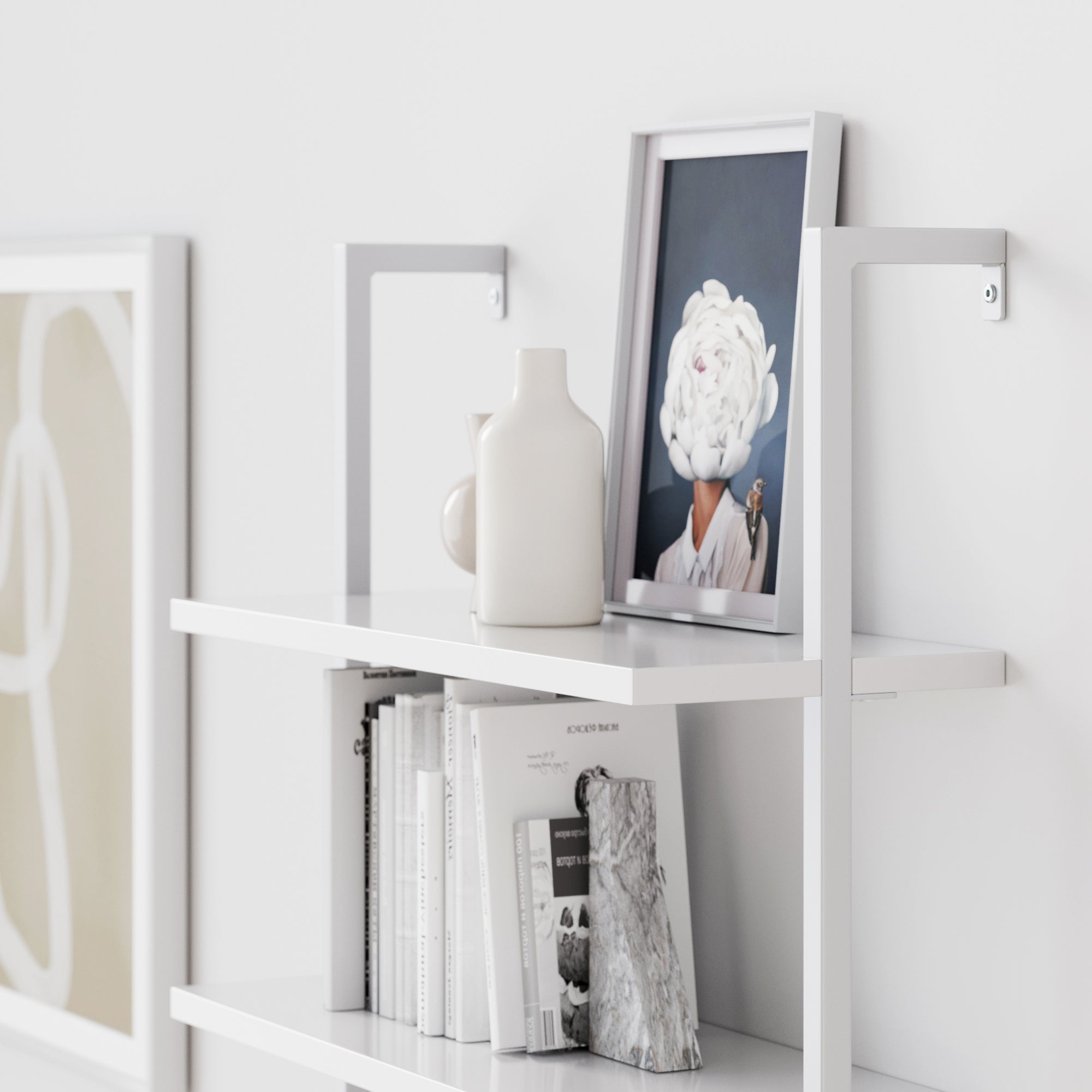 A modern white shelf holds books, two white vases, and a framed photo of a person whose face is obscured by a large white flower. Abstract wall art is partially visible on the wall beside the shelf.