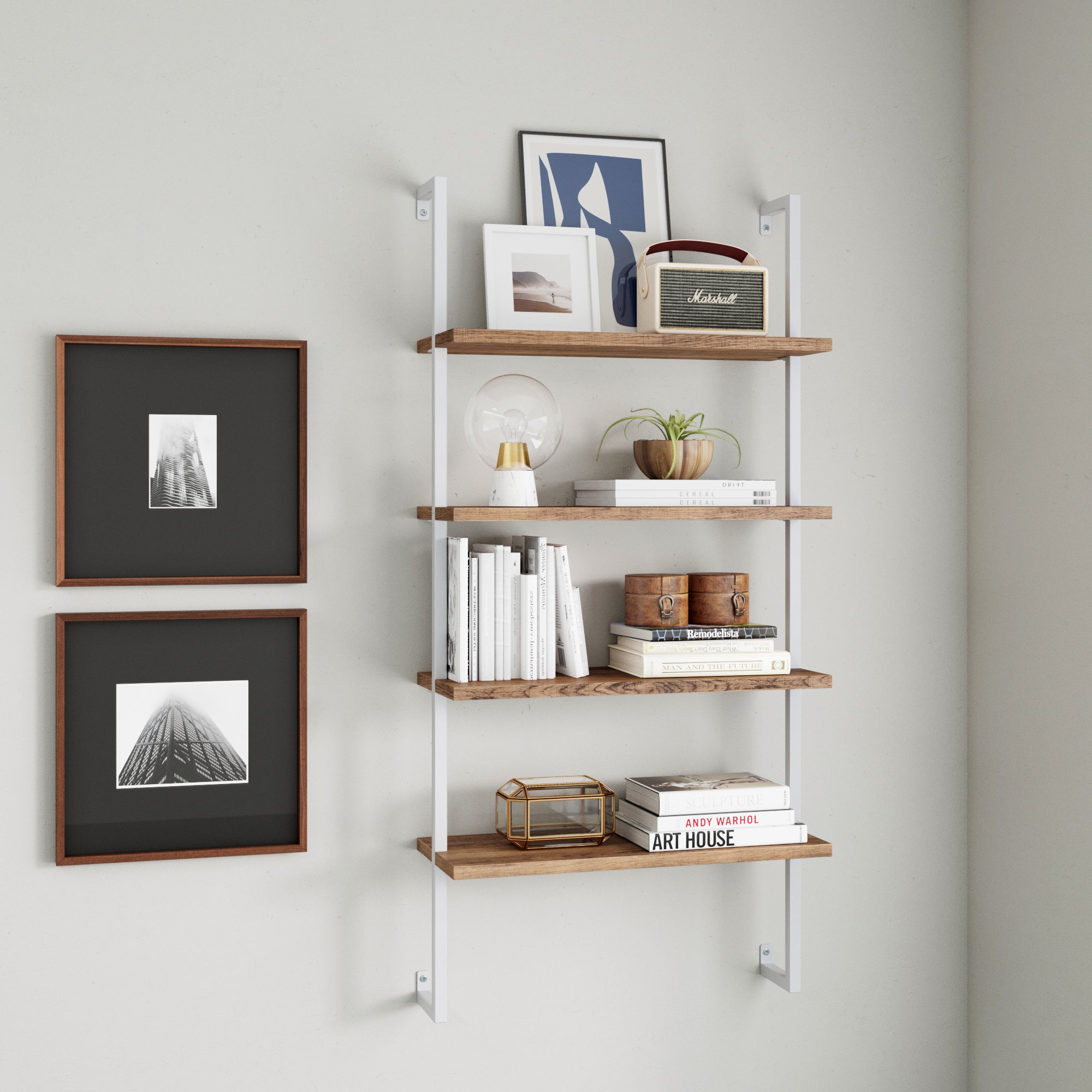 A wall-mounted shelving unit with four wooden shelves holds books, decorative items, a vintage radio, and a framed photo. Two black-and-white framed photos hang on the adjacent white wall.