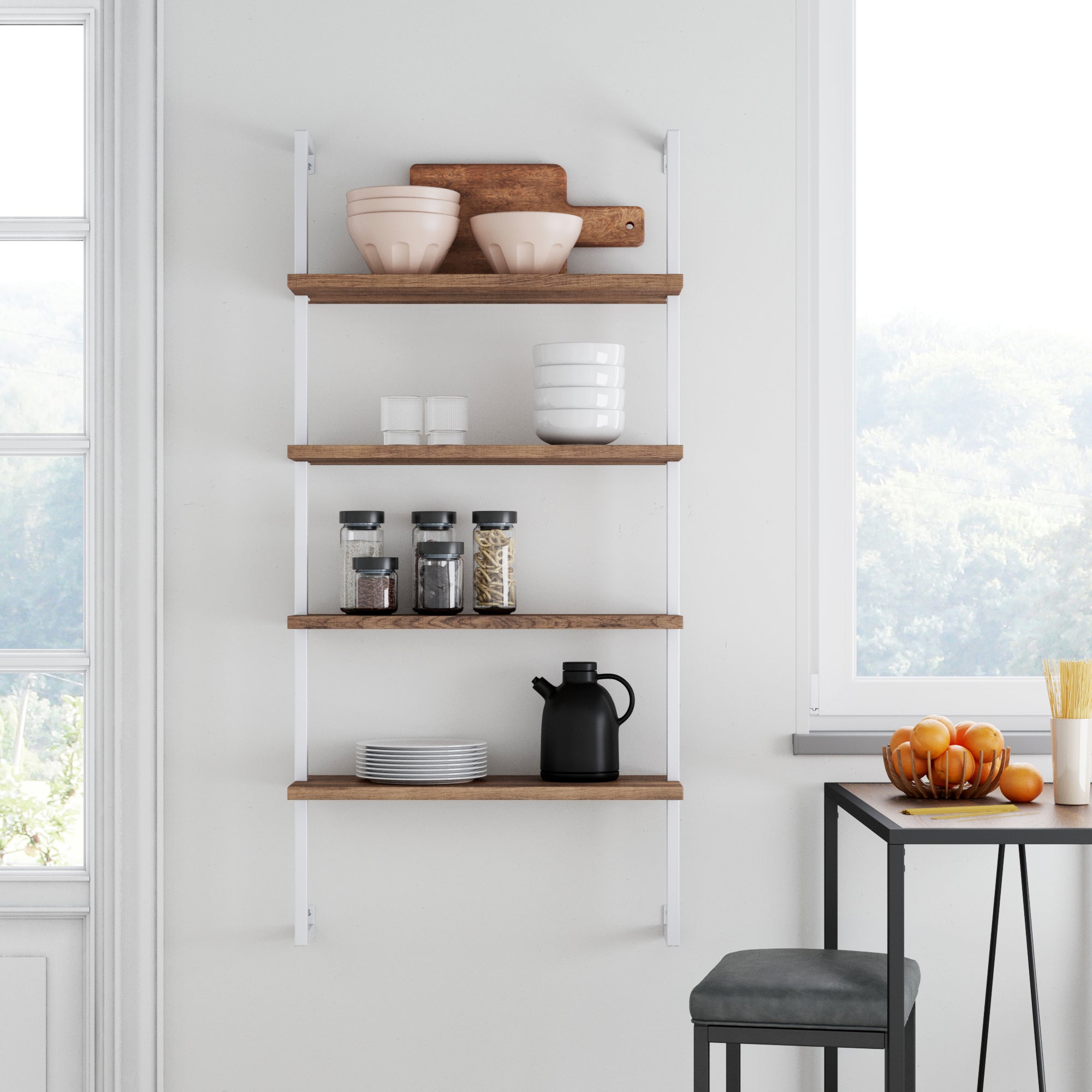 A modern kitchen showcases the Nathan James Wood & Metal 4-Shelf Floating Bookshelf in Reclaimed Oak, displaying bowls, cutting boards, jars, cups, plates, and a black kettle. Nearby, a table with fruit and a stool sit beside sunlit windows.