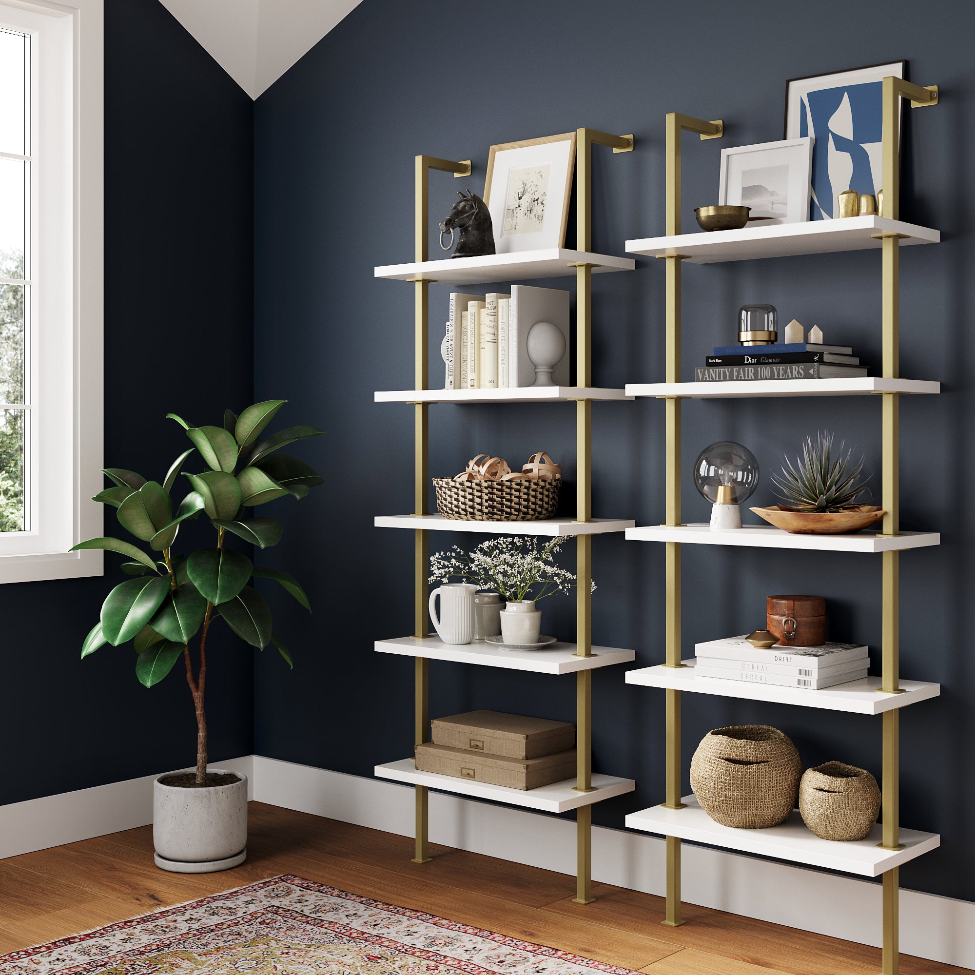 A modern space features the Nathan James 5-Shelf Ladder Wall Bookshelves in white and gold (set of 2) against a dark blue wall, styled with books, art, plants, baskets, and décor. A potted plant by the window rests on a rug over the wood floor.