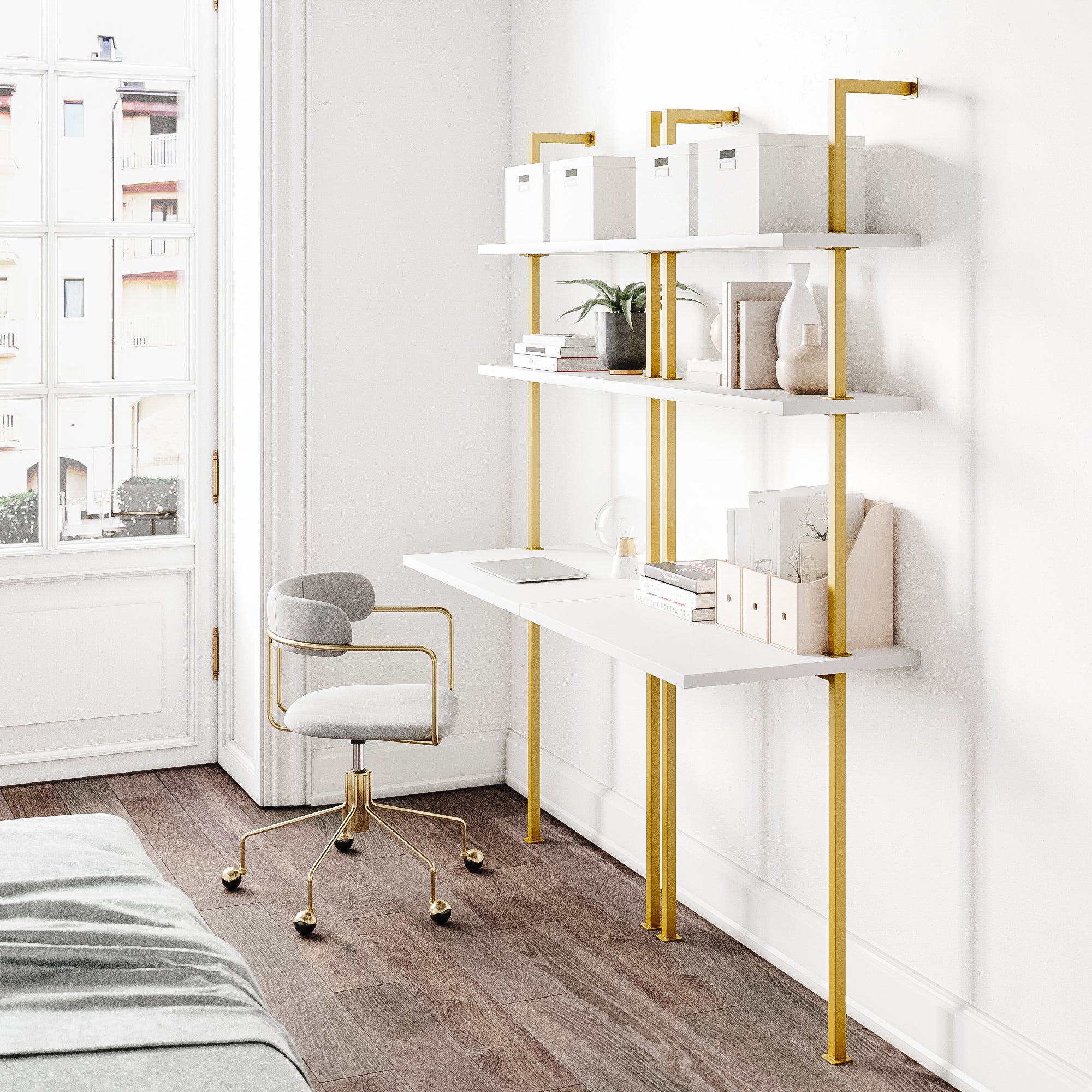 A modern home office features a white desk with gold legs, matching wall shelves holding boxes, books, and decor. A gray and gold chair is in front of the desk, with natural light streaming in from a large window.