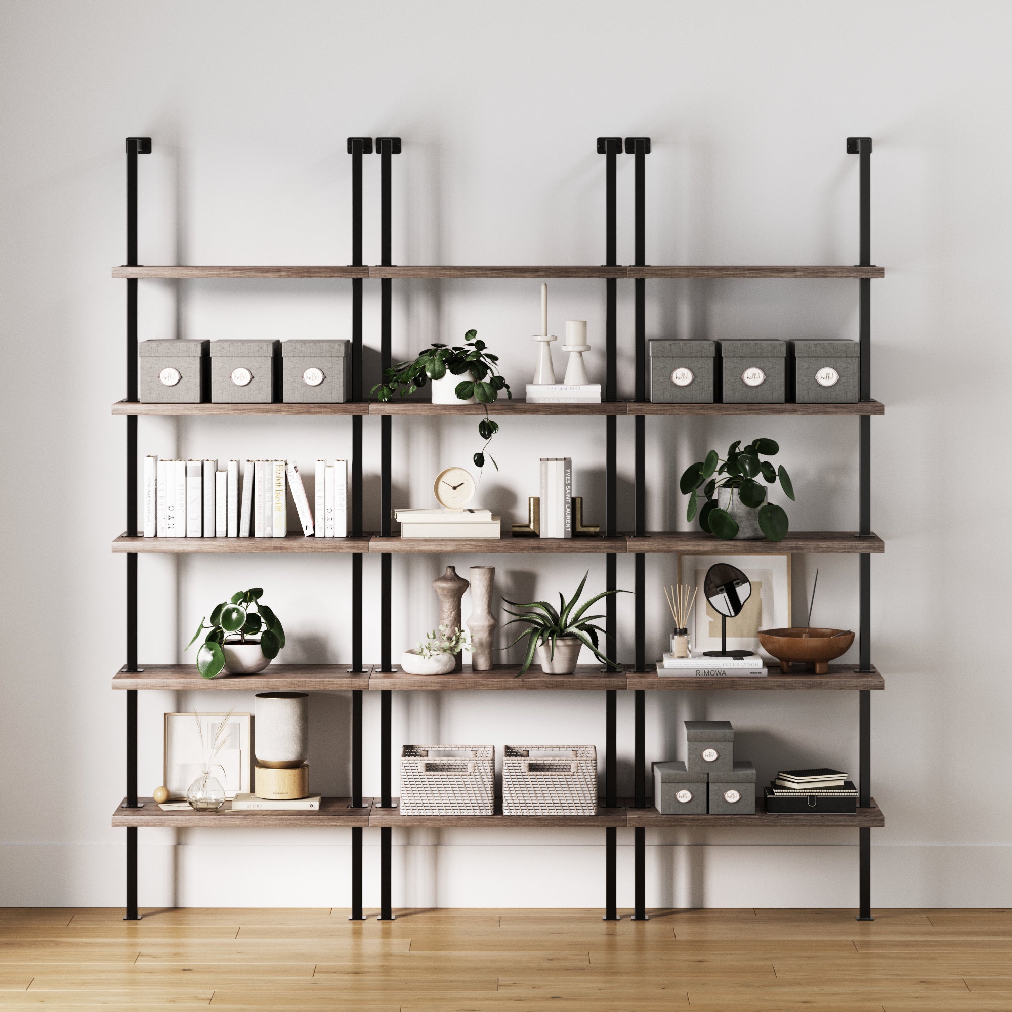 A set of three Nathan James 5-Shelf Ladder Bookshelves in gray oak with black metal supports displays storage boxes, books, potted plants, candles, and baskets against a white wall on a wooden floor.