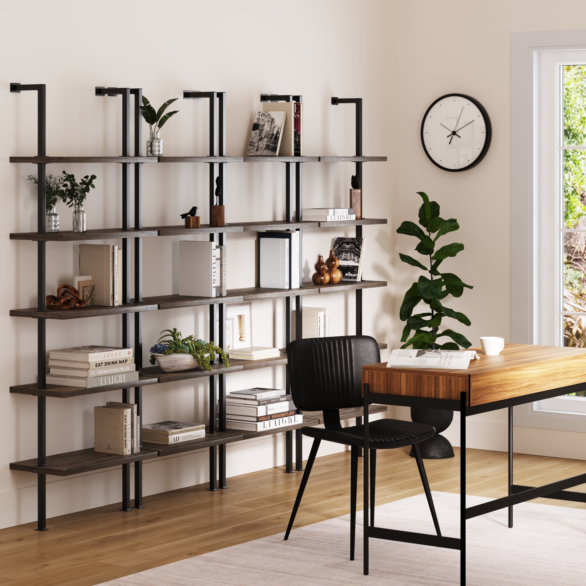A modern home office with a wooden desk, black chair, four Nathan James 5-Shelf Ladder Bookshelves in gray oak holding books and decor, a potted plant, wall clock, and sunlight streaming through the window.