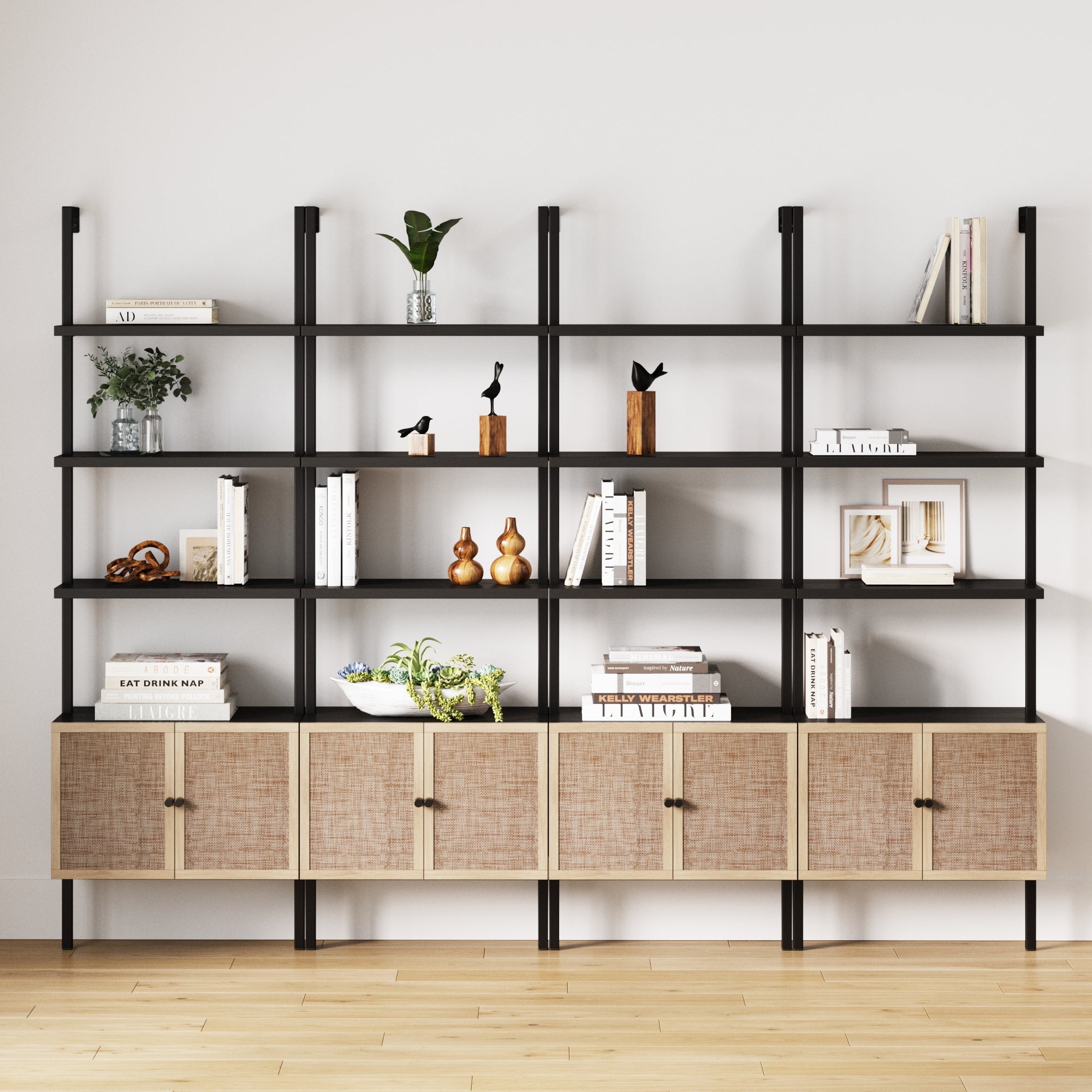 A modern black metal and wood bookshelf with cabinets displays books, plants, decorative birds, and small sculptures against a plain white wall on a light wood floor.