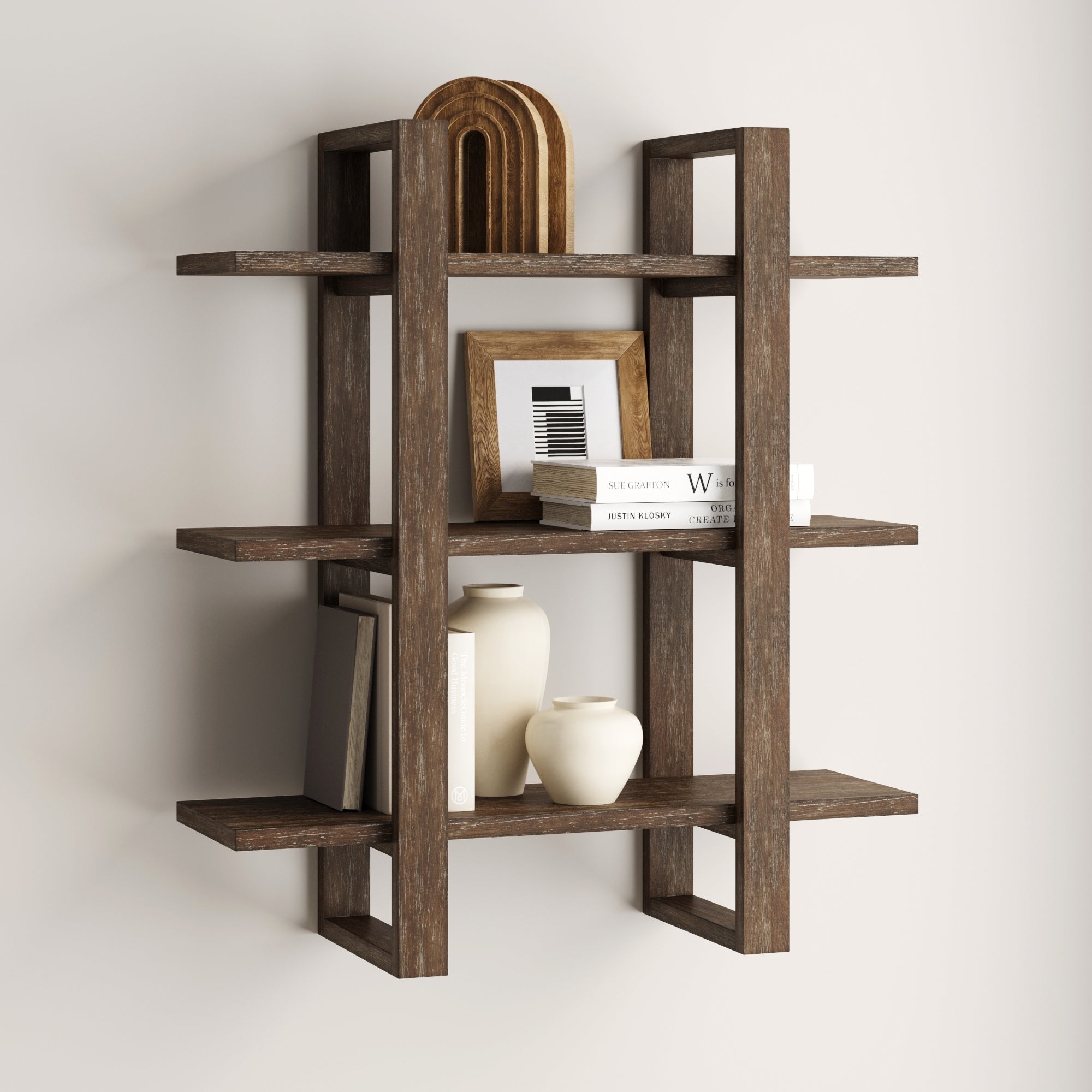 The Nathan James Solid Wood Adjustable Wall Shelf in dark brown features a modern geometric design, displaying vases, books, a framed photo, and wooden arches against a light-colored wall.