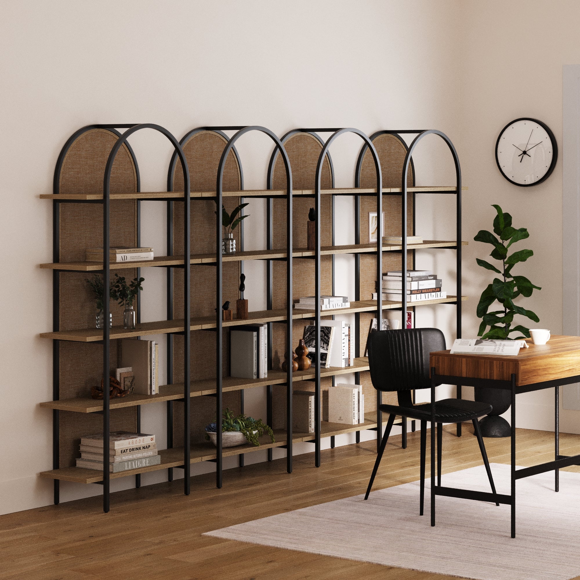 A modern office features a wooden desk, black chair, and Nathan James Boho Rattan & Wood Arched Bookshelves (Set of 4) filled with books and decor, plus a potted plant, wall clock, and light walls and flooring.