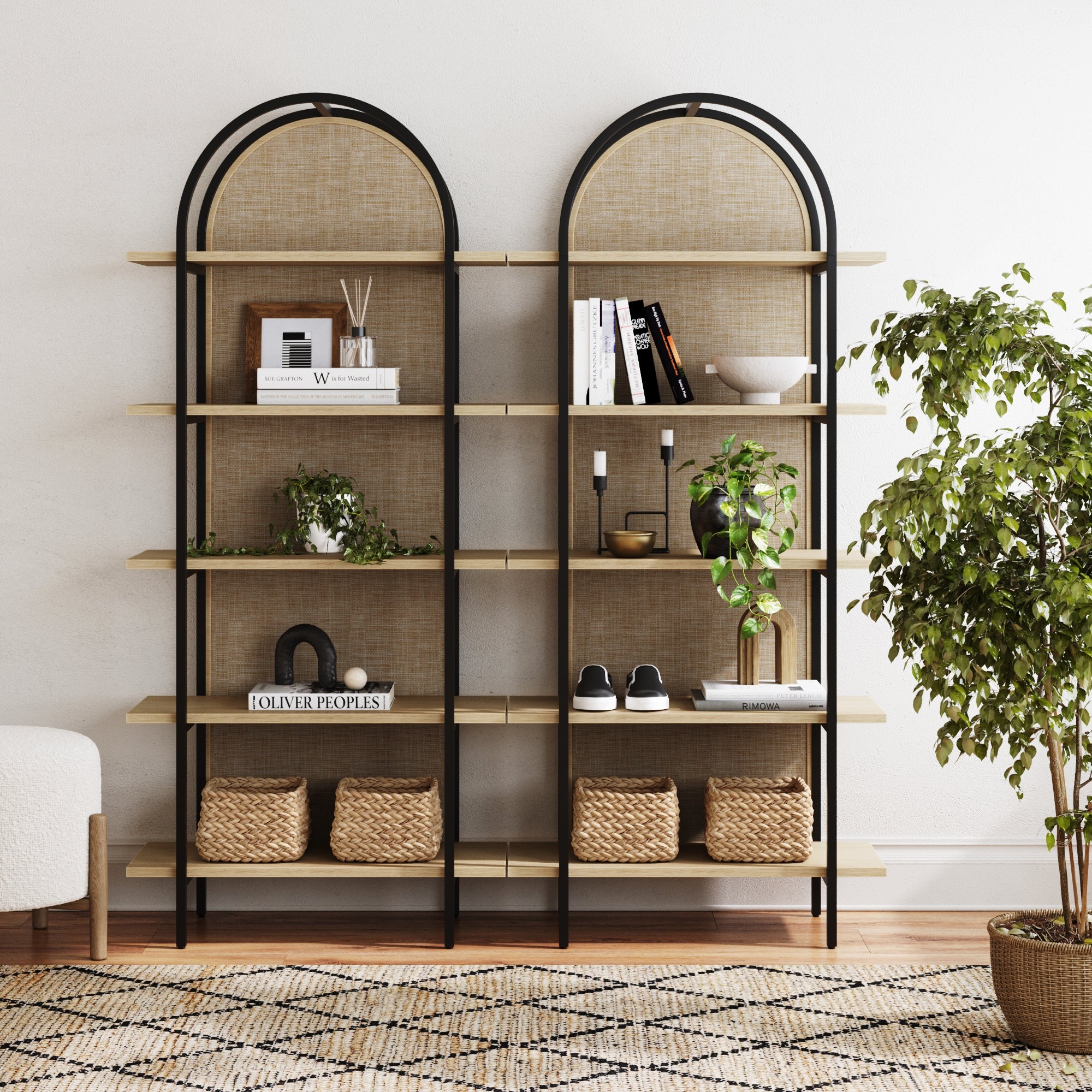 Two tall arch-shaped shelves hold books, plants, baskets, and decor items, set against a light wall. A leafy potted plant is on the right, and a patterned rug covers the floor in front.