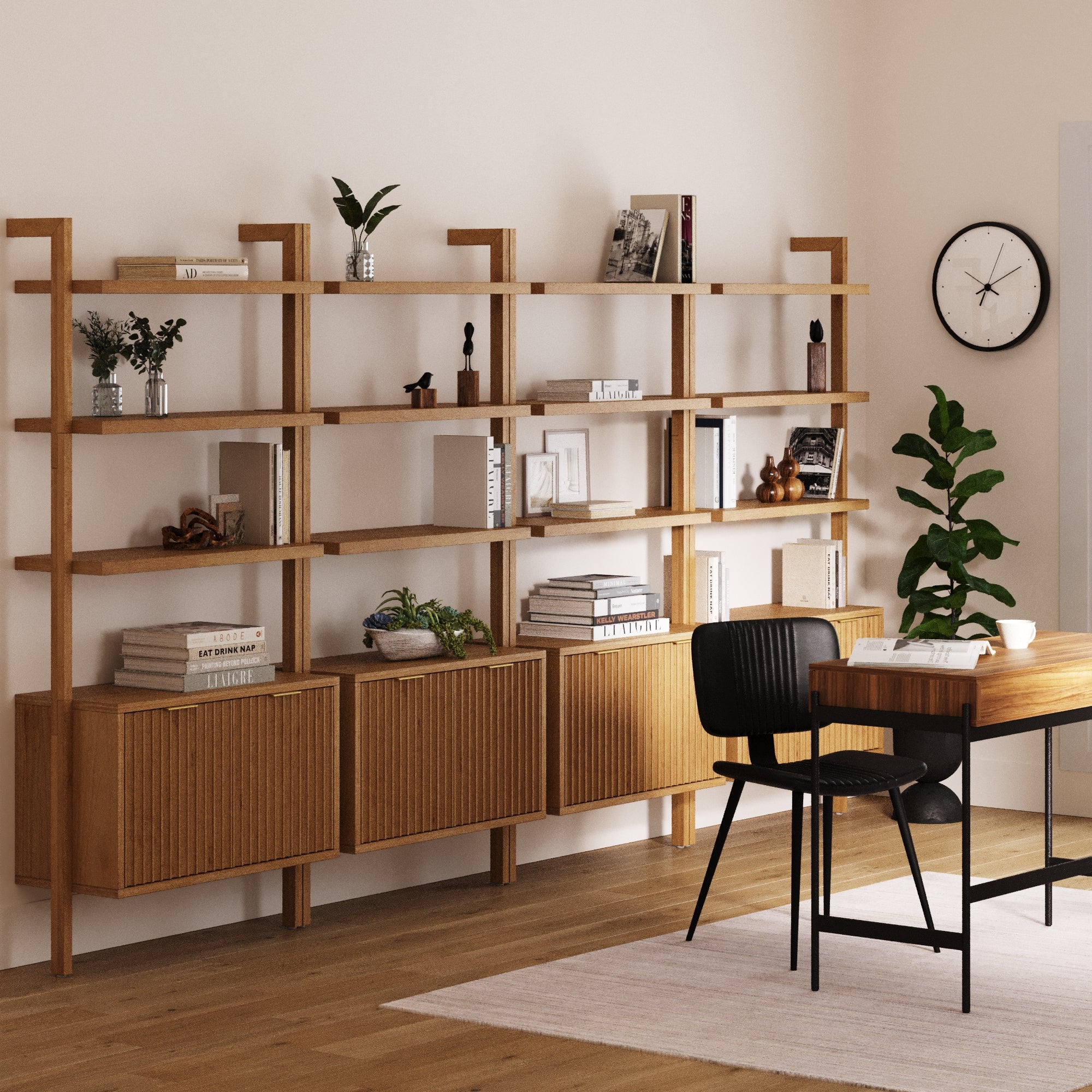 A modern home office features Nathan James Mid-Century Fluted Wall Bookshelves with Doors in Warm Pine (Set of 4), displaying books, decor, and plants, paired with a wooden desk, black chair, potted plant, wall clock, and cozy rug.