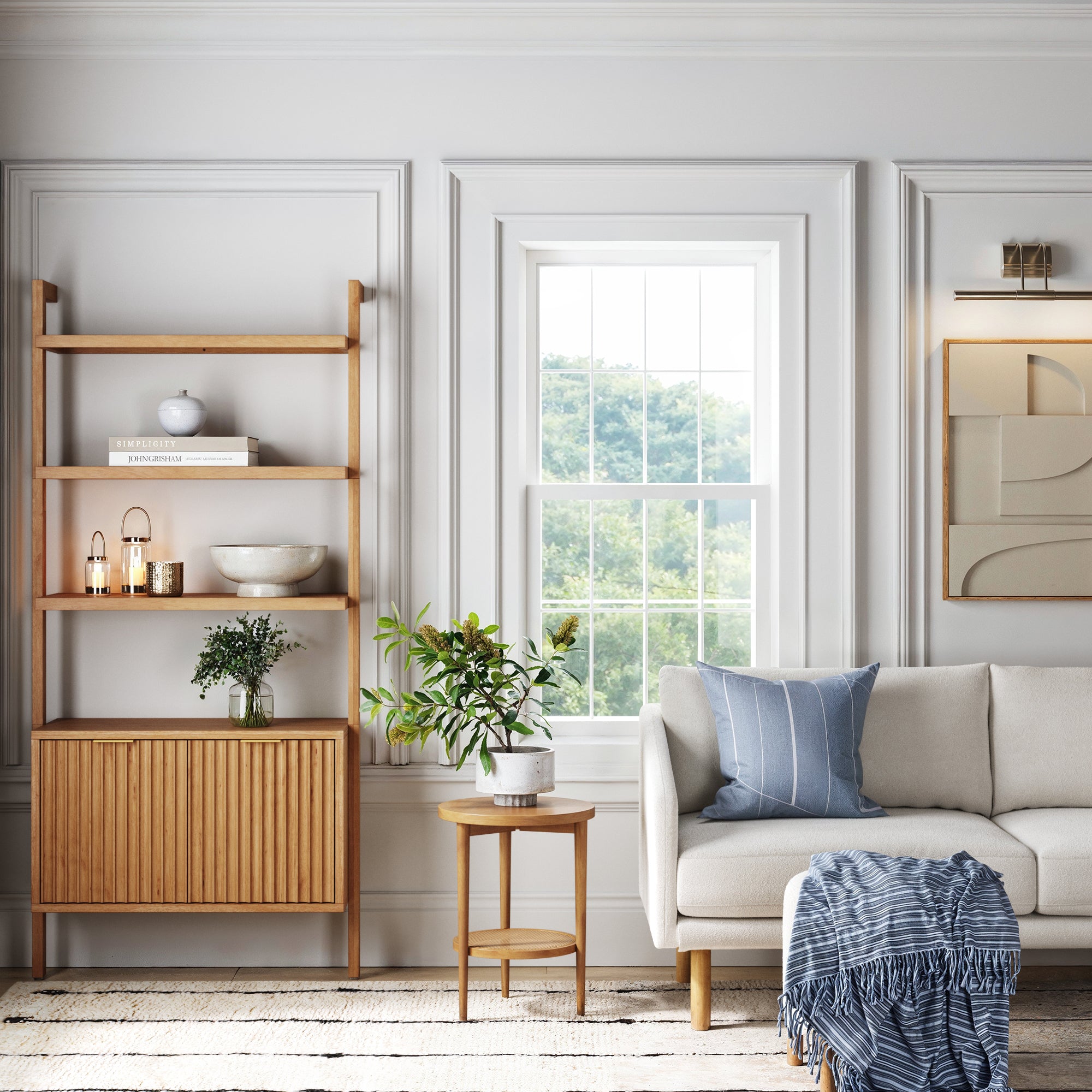 Bright living room with white walls, a window showing greenery outside, wooden shelves with decor, a small side table with a plant, and a white sofa with blue accents and a throw blanket draped over the armrest.