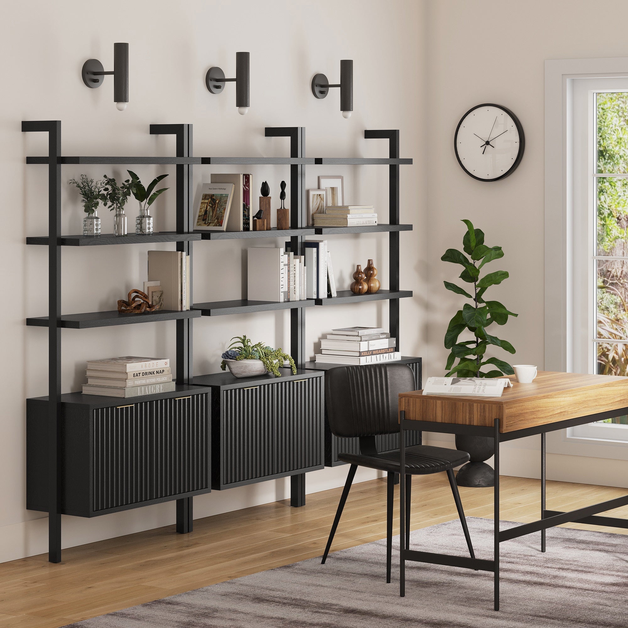 A modern home office features Nathan James Mid-Century Fluted Wall Bookshelves with Doors Black (Set of 3), a wooden desk with black chair, potted plant by the window, and three wall-mounted lights above the shelves.