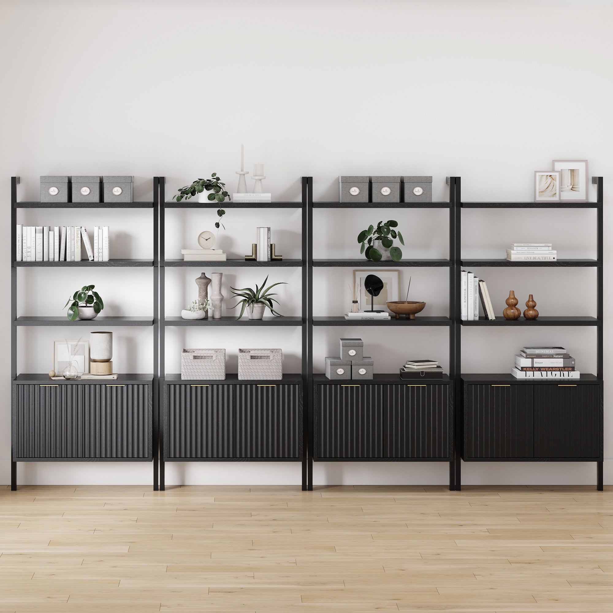 Four Nathan James Mid-Century Fluted Wall Bookshelves with Doors in black stand against a white wall on a light wood floor, styled with books, plants, boxes, and decor.